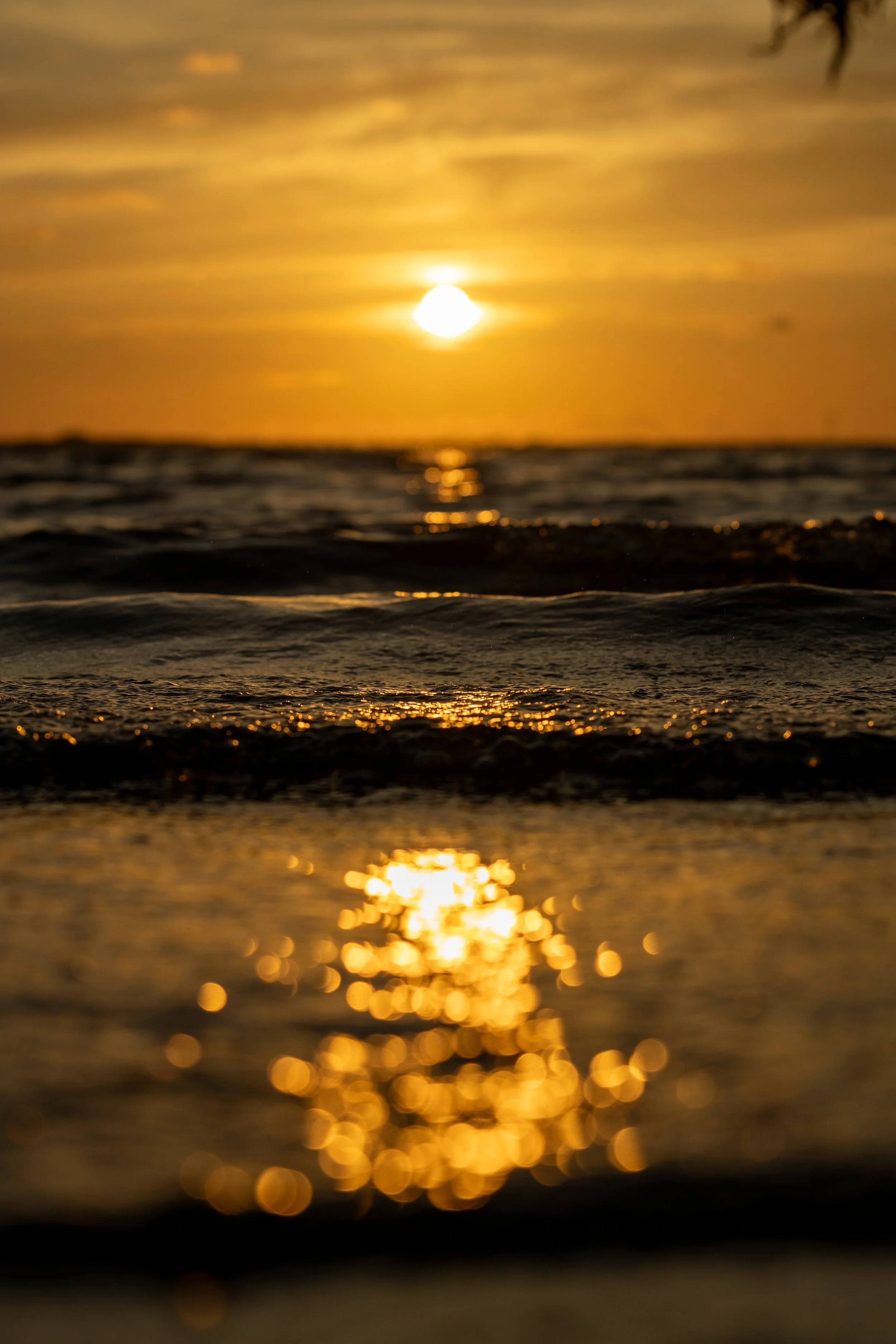 Sunset over the ocean with reflections on the water surface and blurred warm tones in the background.