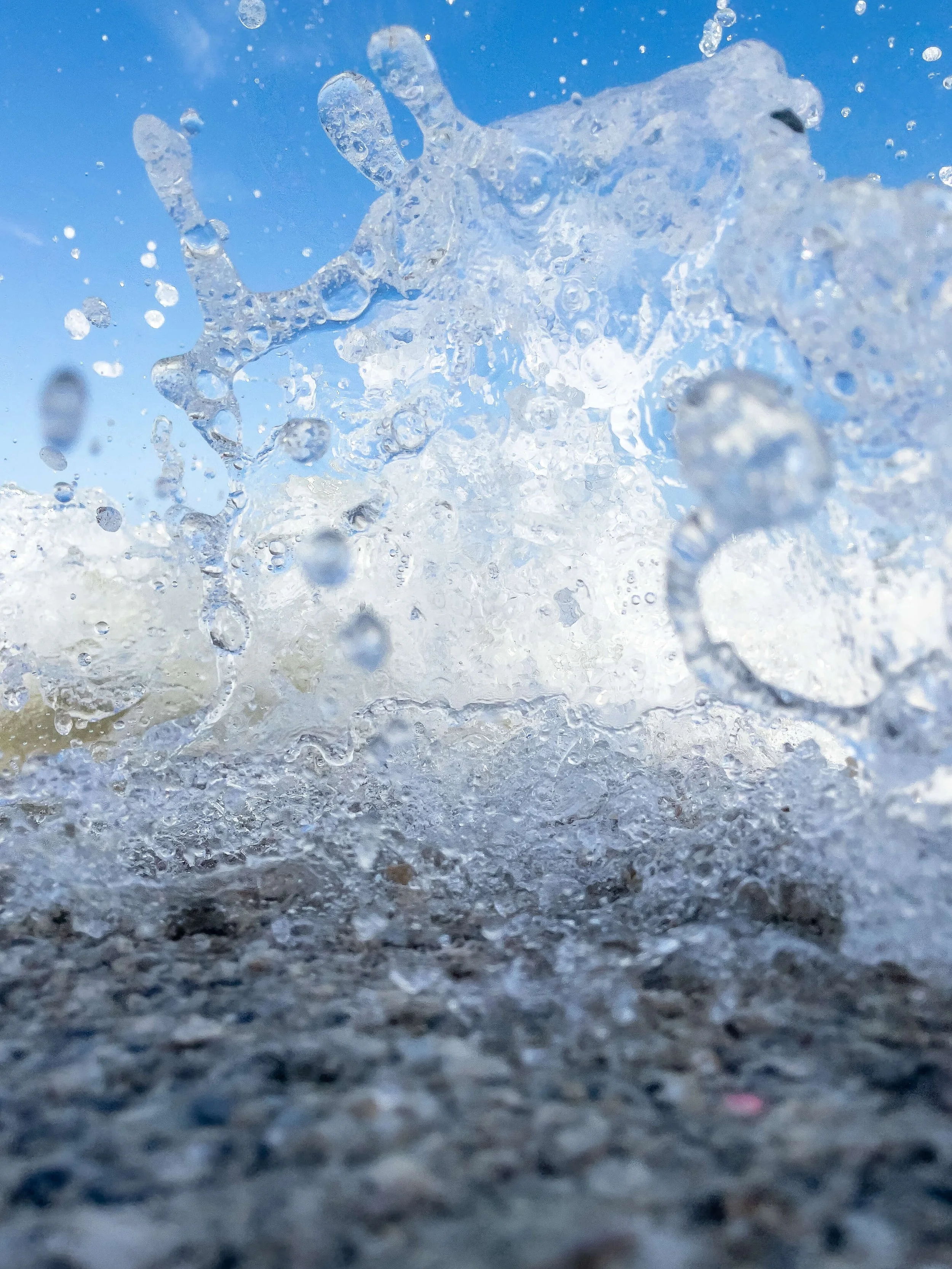 Close-up of water splashing on a sandy surface with a blue sky background.