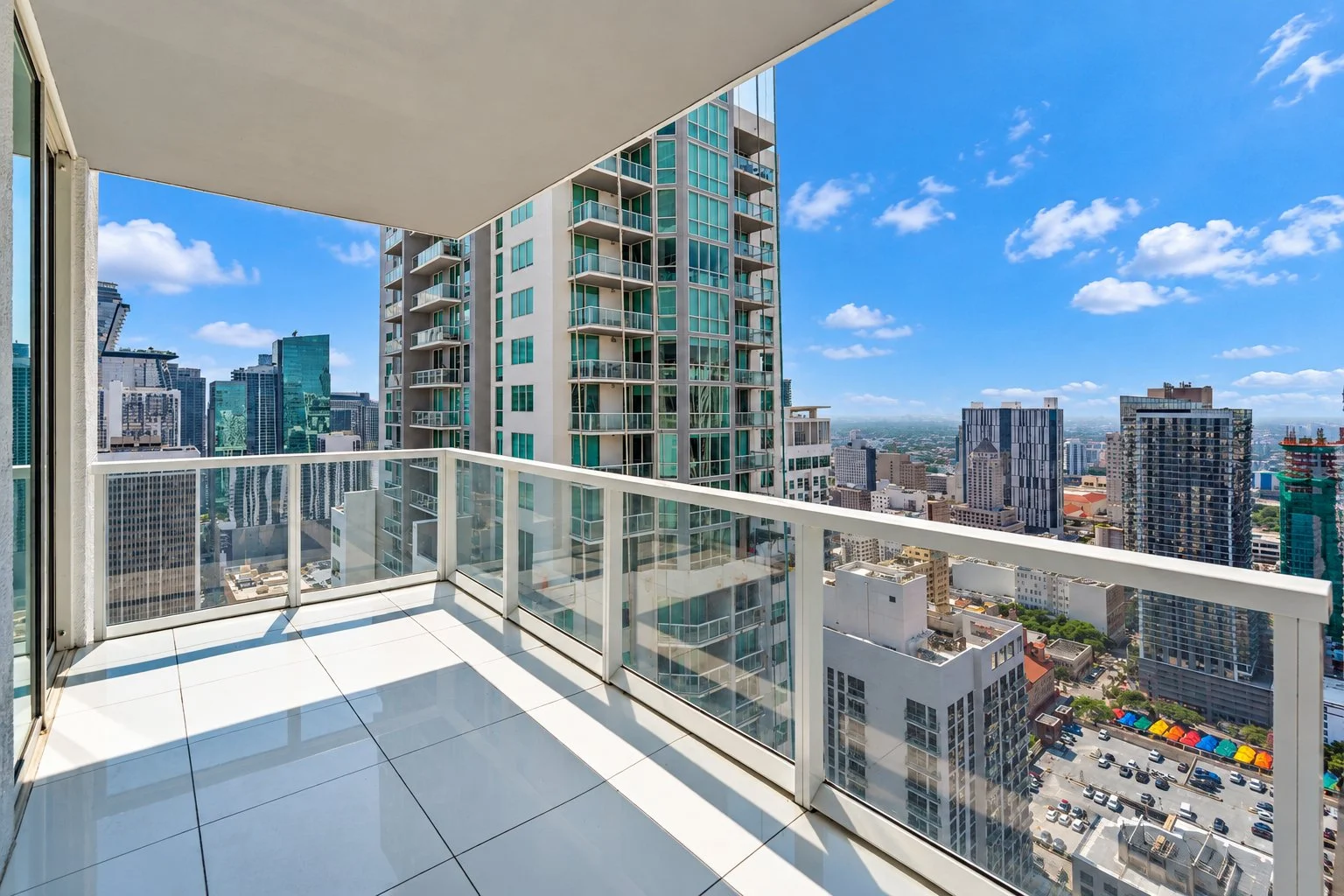 View from a balcony of a high-rise apartment with city skyscrapers under a blue sky with scattered clouds.