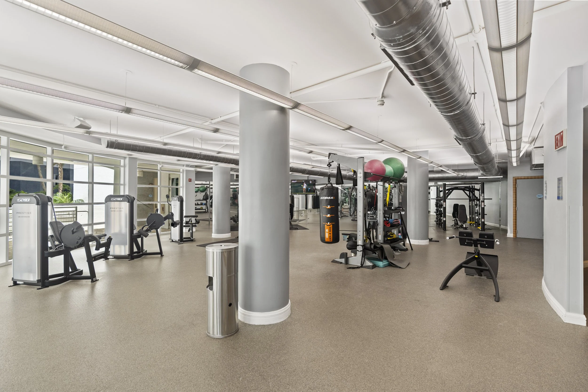 Interior of a modern gym with workout equipment, exercise machines, weight stations, stability balls, and bright lighting.