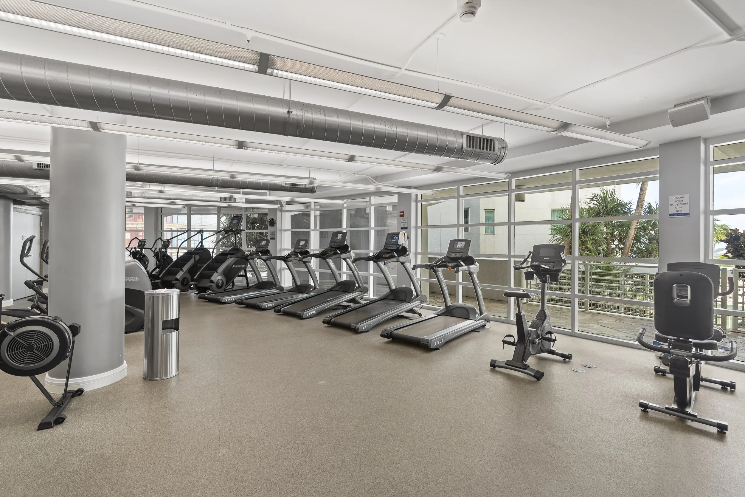 Fitness center with treadmills, ellipticals, and exercise equipment near large windows with outdoor view.