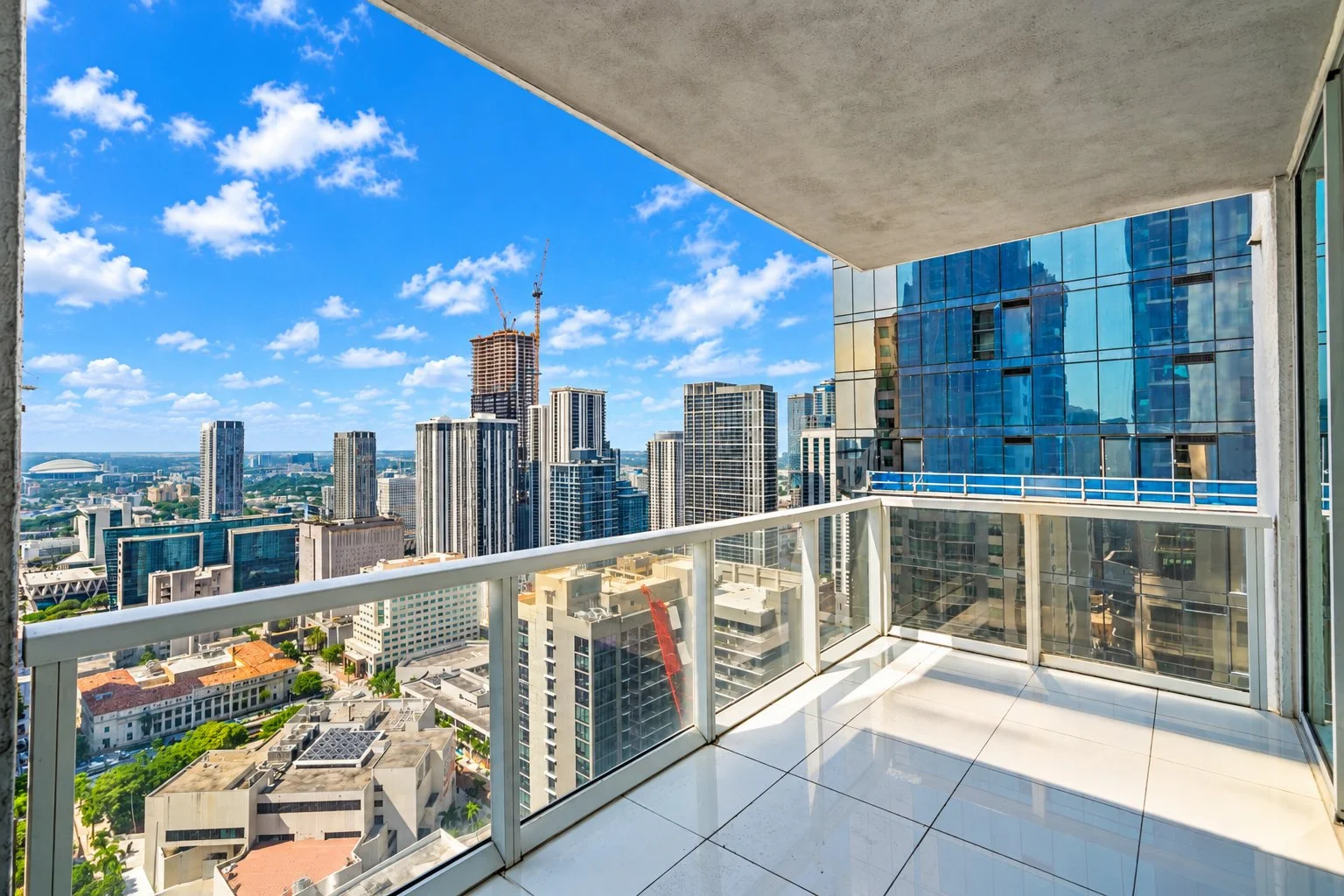 Empty balcony with glass railing overlooking a city skyline with tall skyscrapers under a partly cloudy sky.