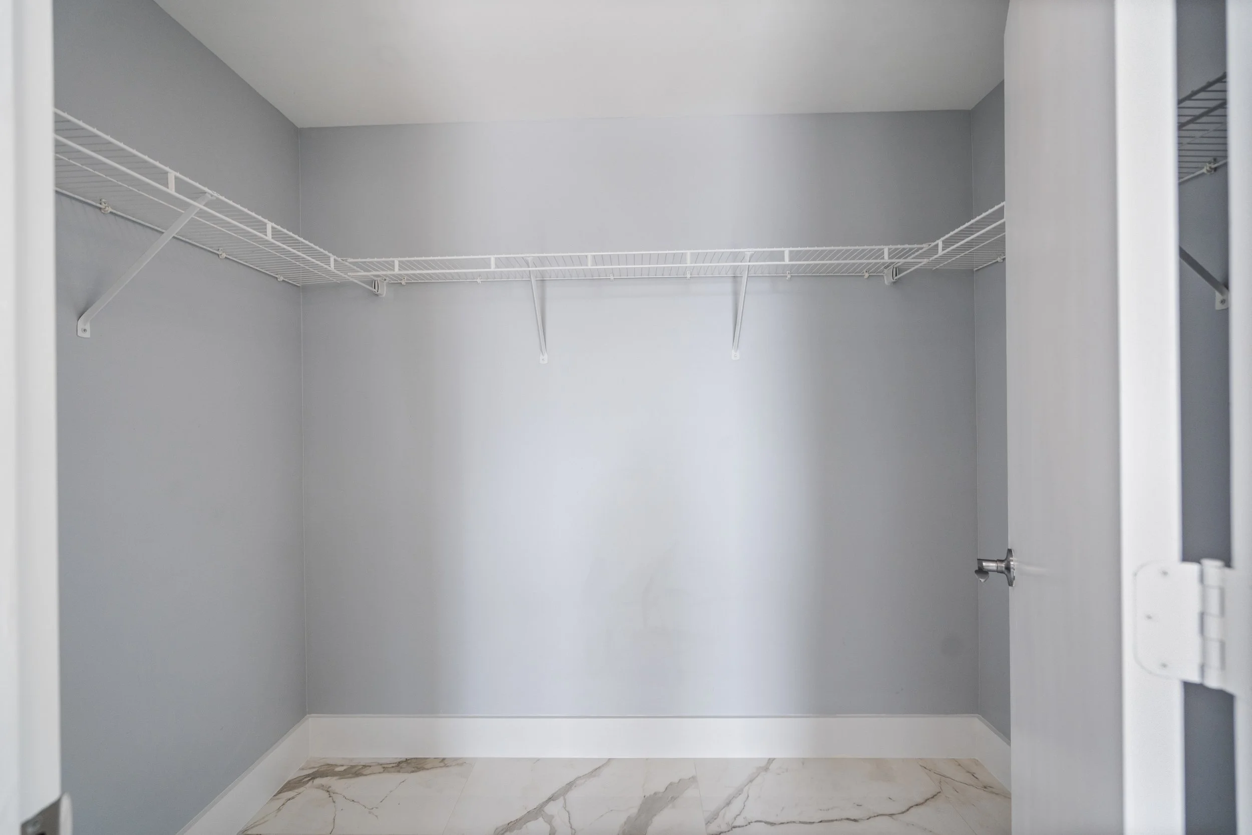 Empty closet with gray walls, white wire shelves, and marble-look tile floor.
