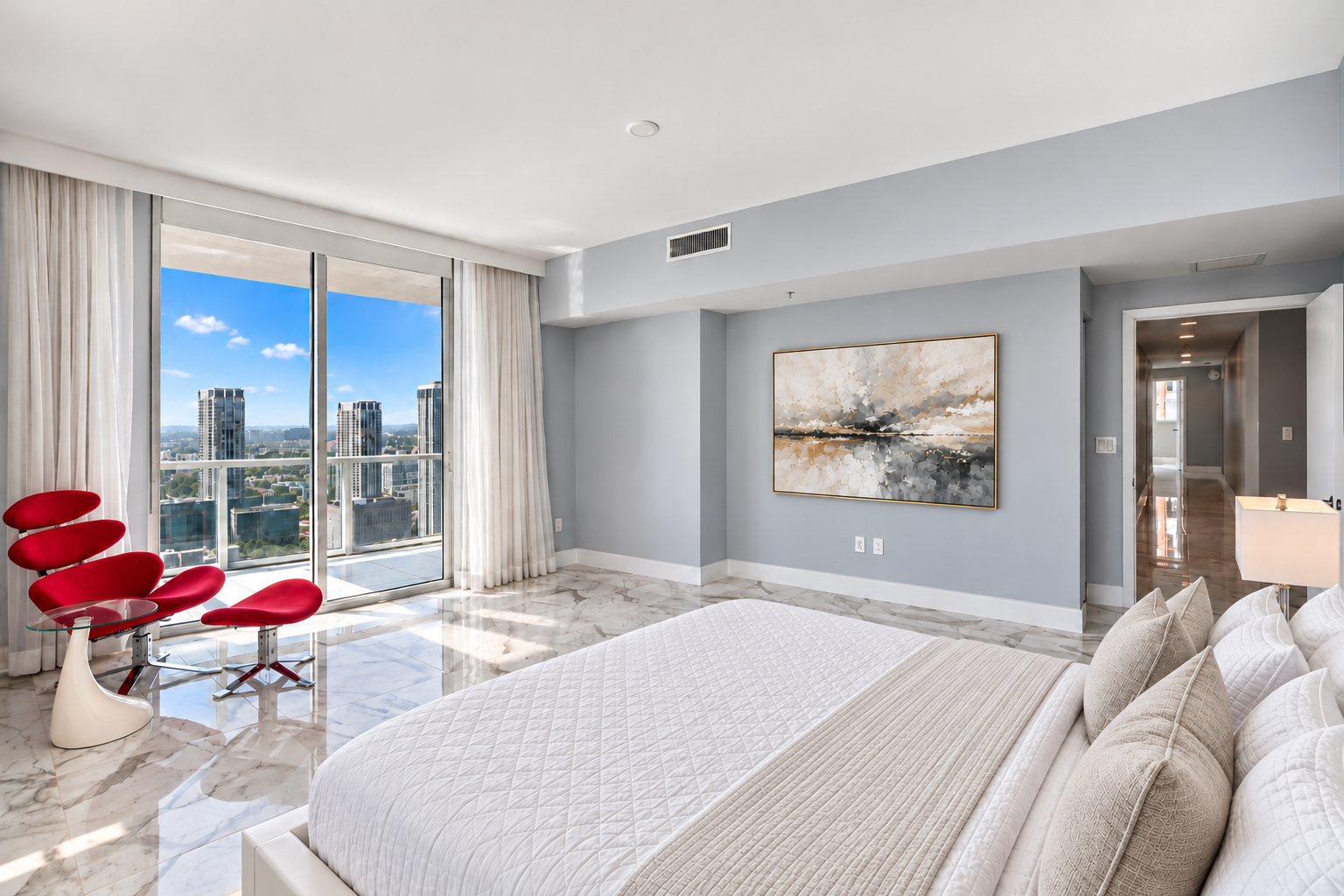 Modern bedroom with a large window, city view, white marble floor, white bed with beige bedding, red chair, and abstract artwork on the wall.