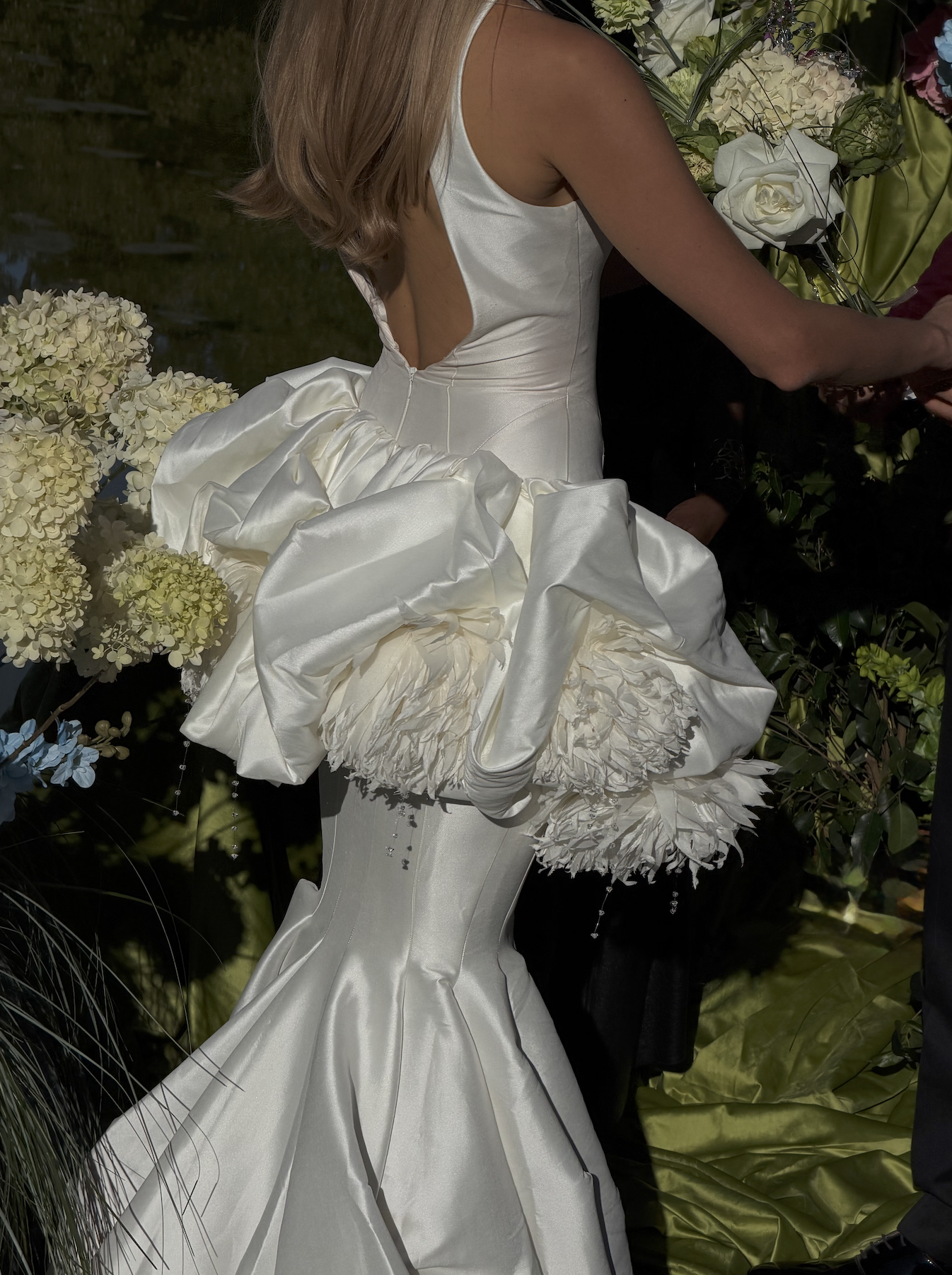 Une femme portant une robe de mariée blanche en satin avec des détails en froufrous, entourée de fleurs.