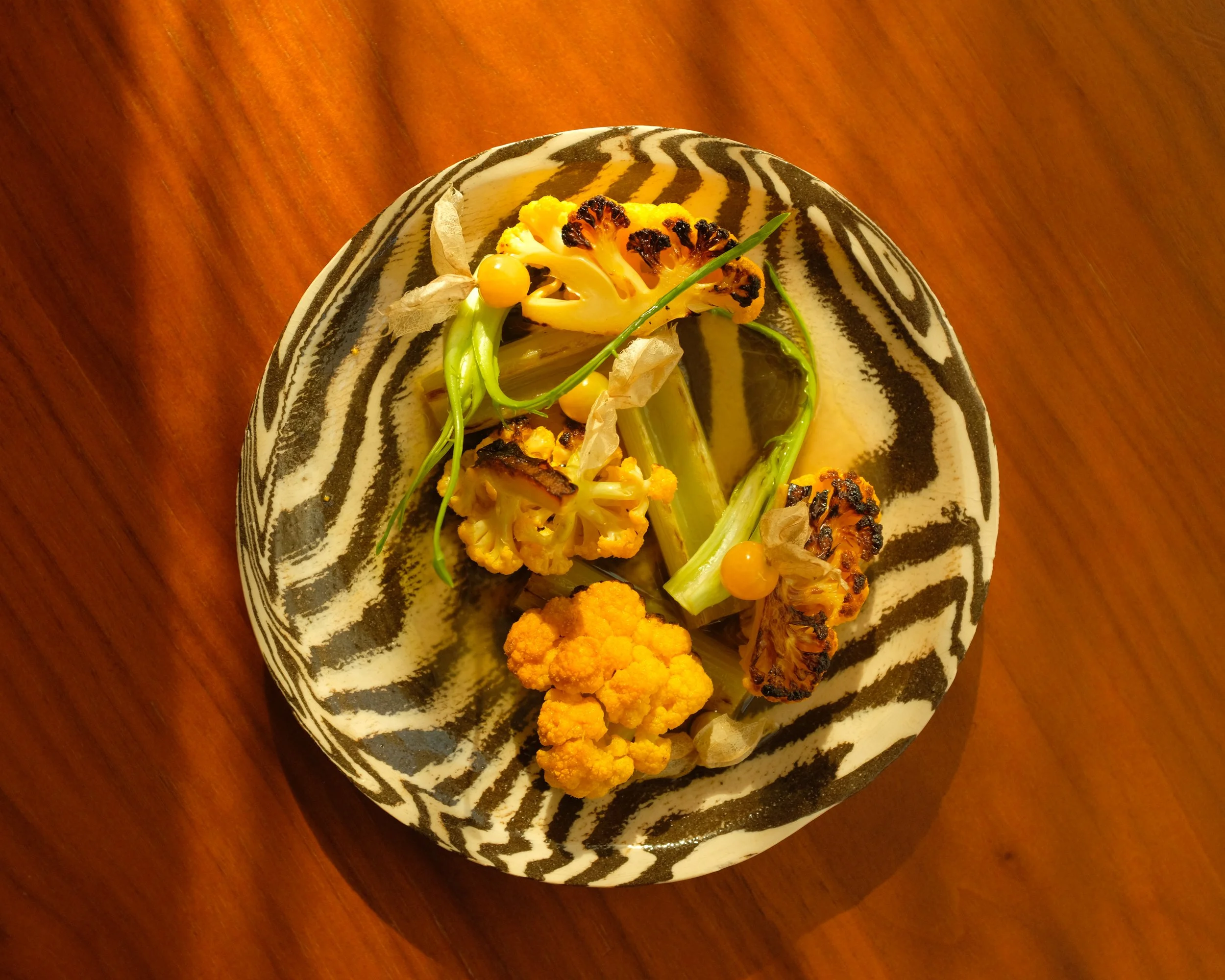 Overhead view of roasted cauliflower and vegetables garnished with cape gooseberries on a black-and-white patterned plate