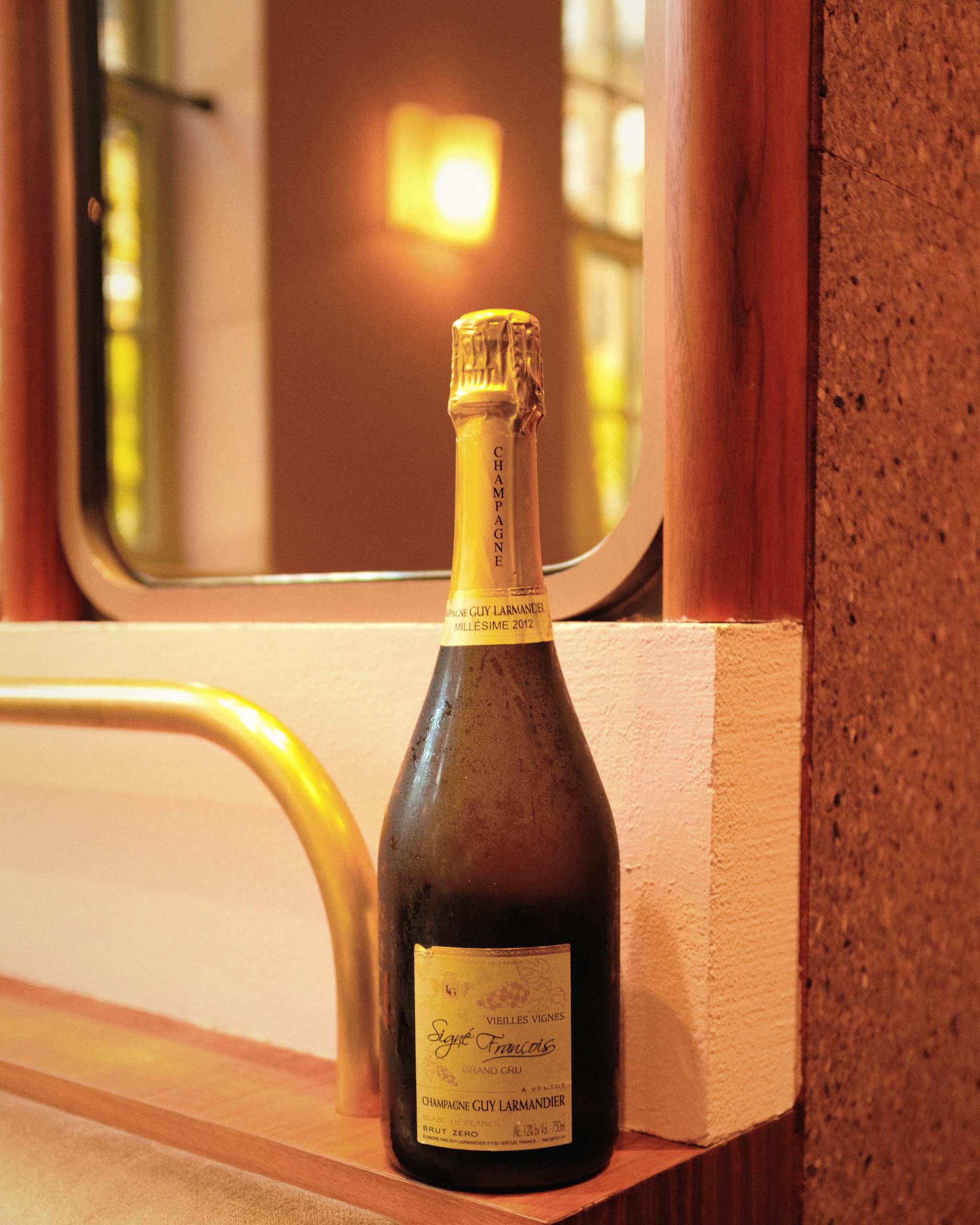 Bottle of Champagne Guy Larmandier Blanc de Blancs Brut Zero Grand Cru displayed on a warmly lit windowsill.