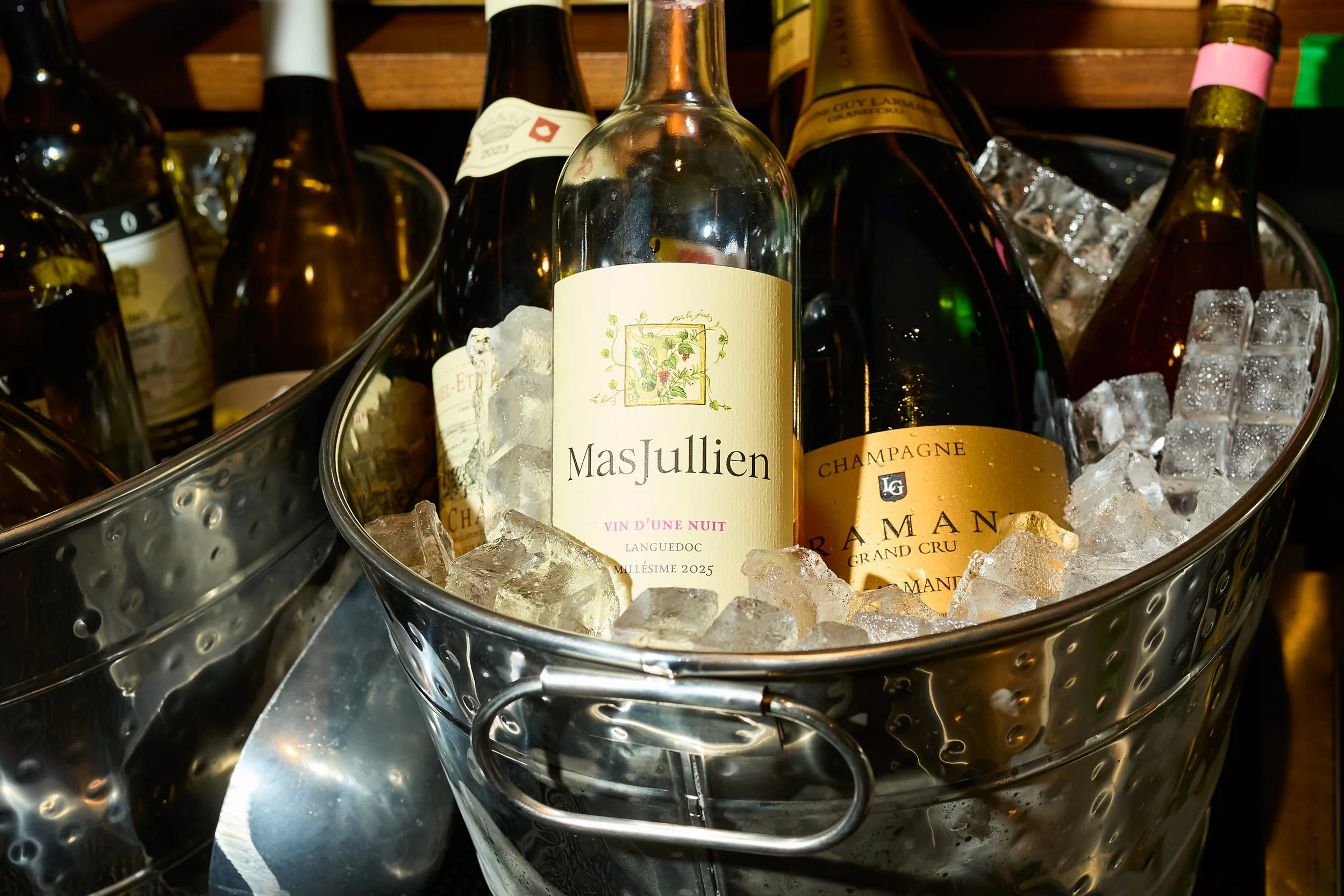 Bottles of wine and champagne chilling in ice-filled metal buckets at a bar.