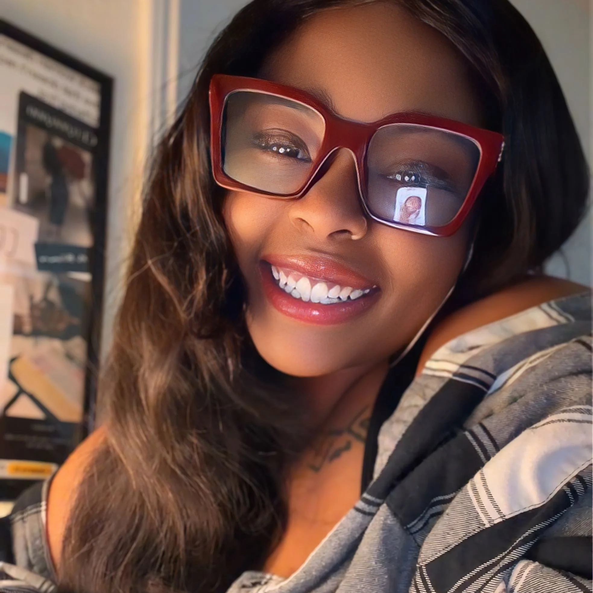 A woman wearing large red sunglasses smiling in a store, with shelves and products in the background.