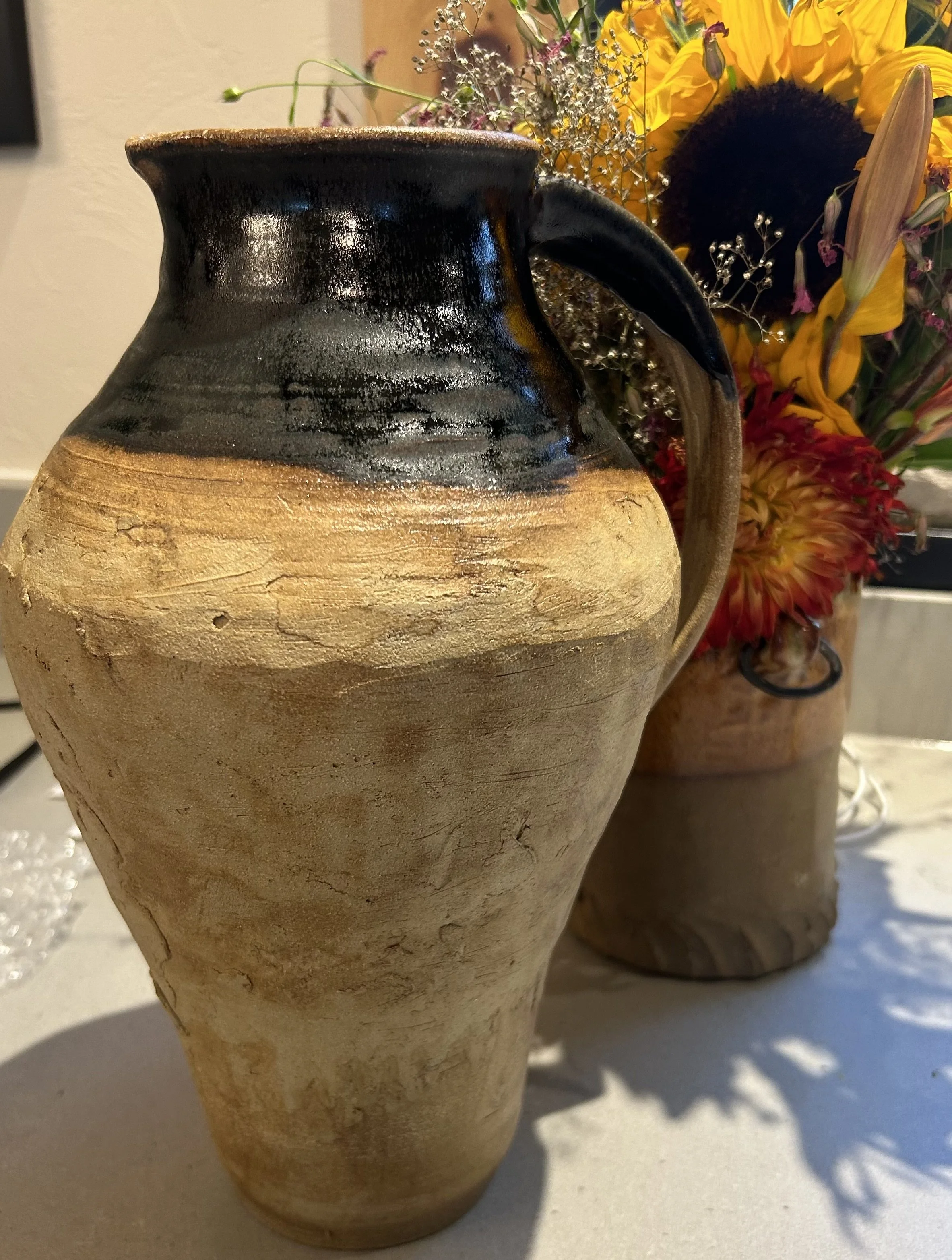 Tall handmade ceramic vase with textured natural clay, dark glaze and flowers by Catherine Hauser.