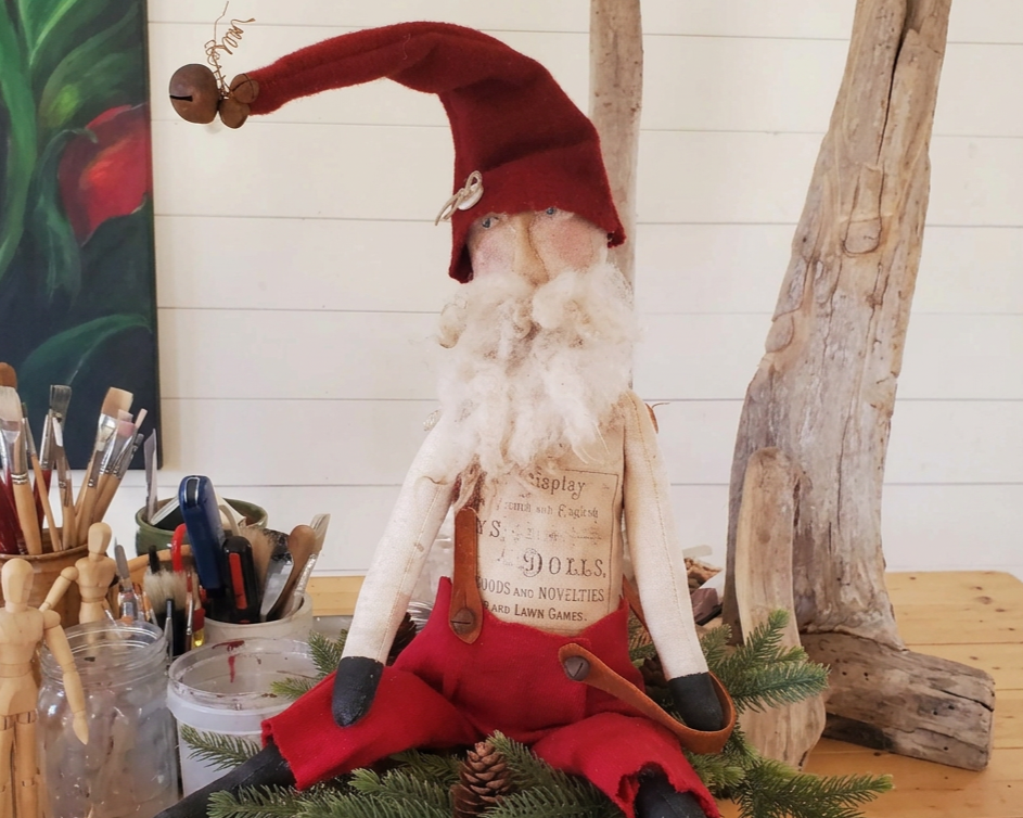 Handmade folk-art Santa with a long red pointed hat, vintage-style fabric clothing and a curly white beard.