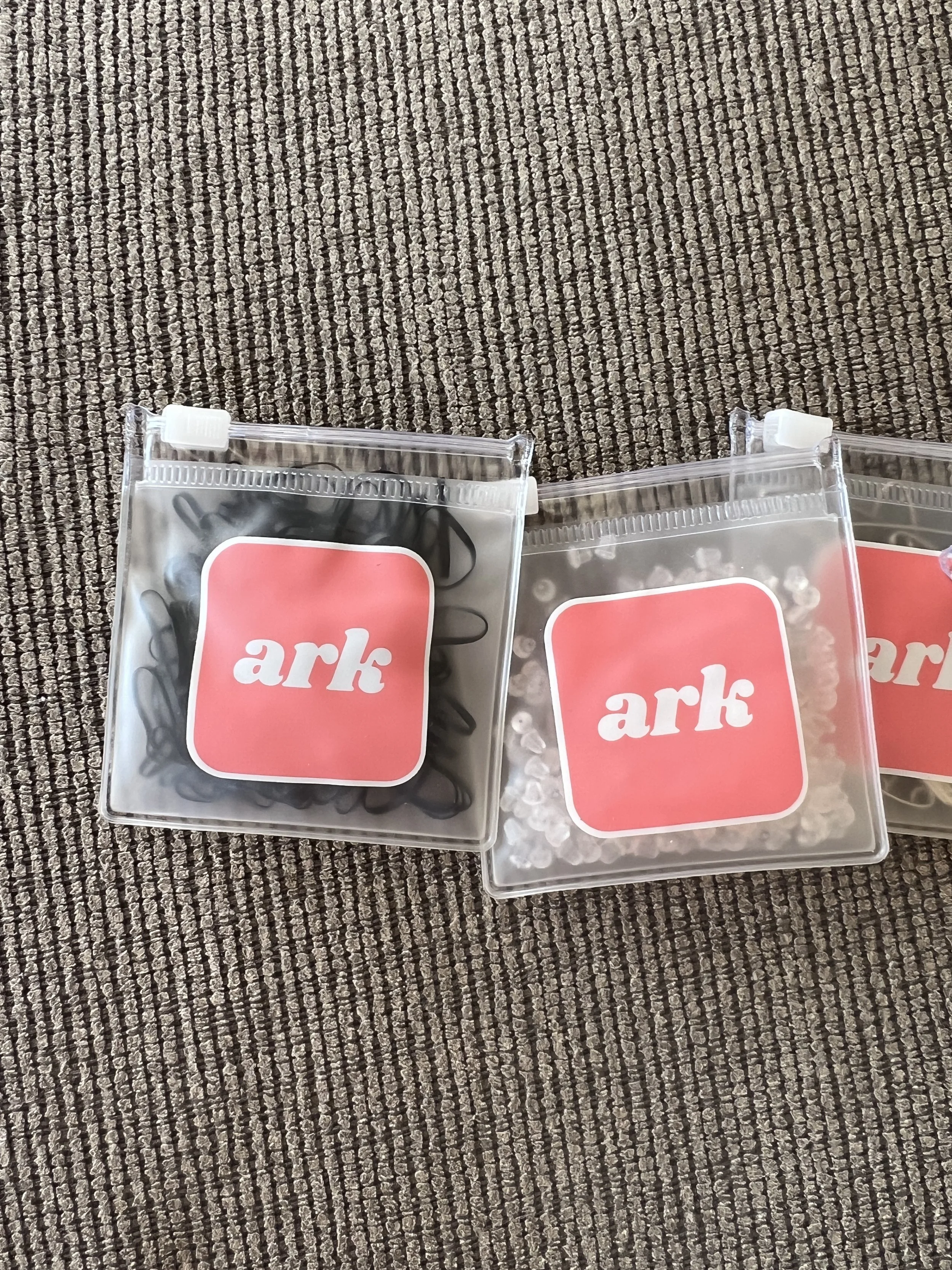 Three small plastic bags labeled 'ark' with different contents, placed on a textured brown carpet.