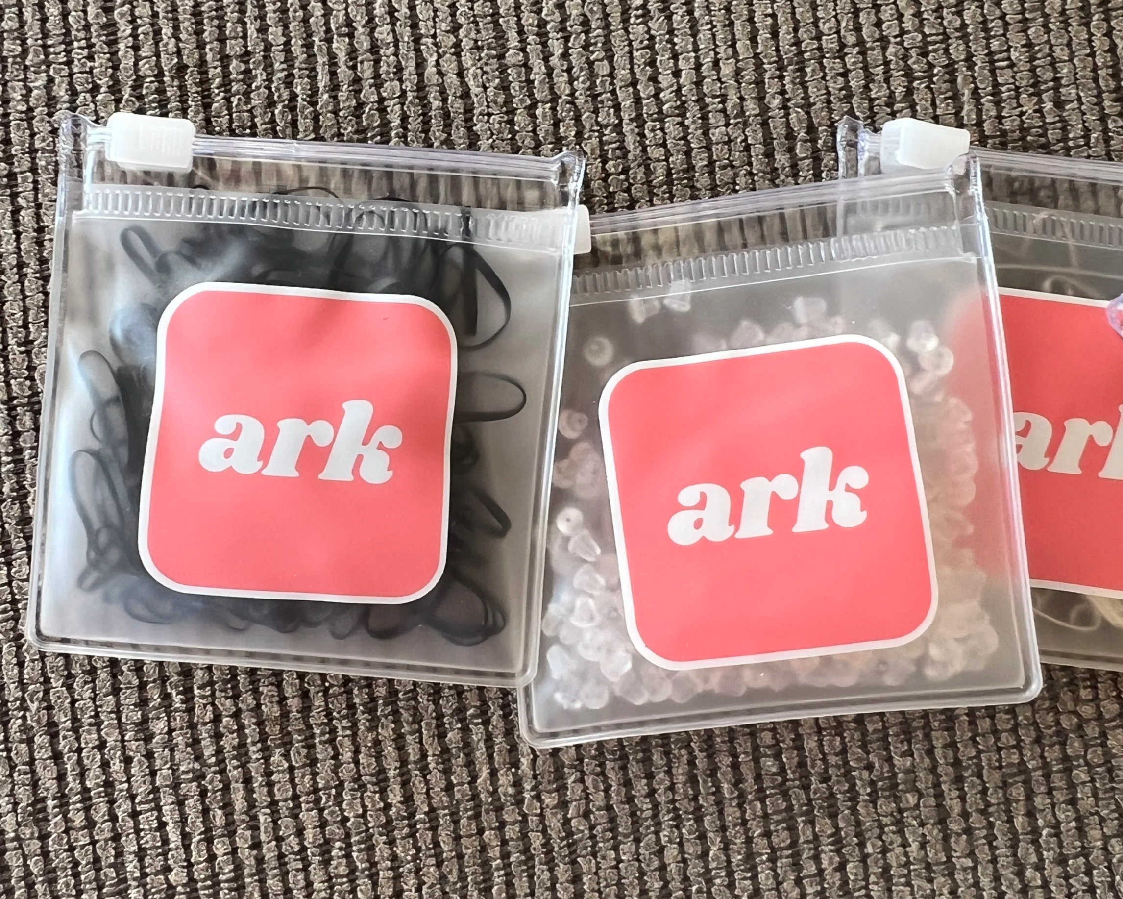 Three sealed plastic packages with pink and white labeling placed on a textured gray surface.
