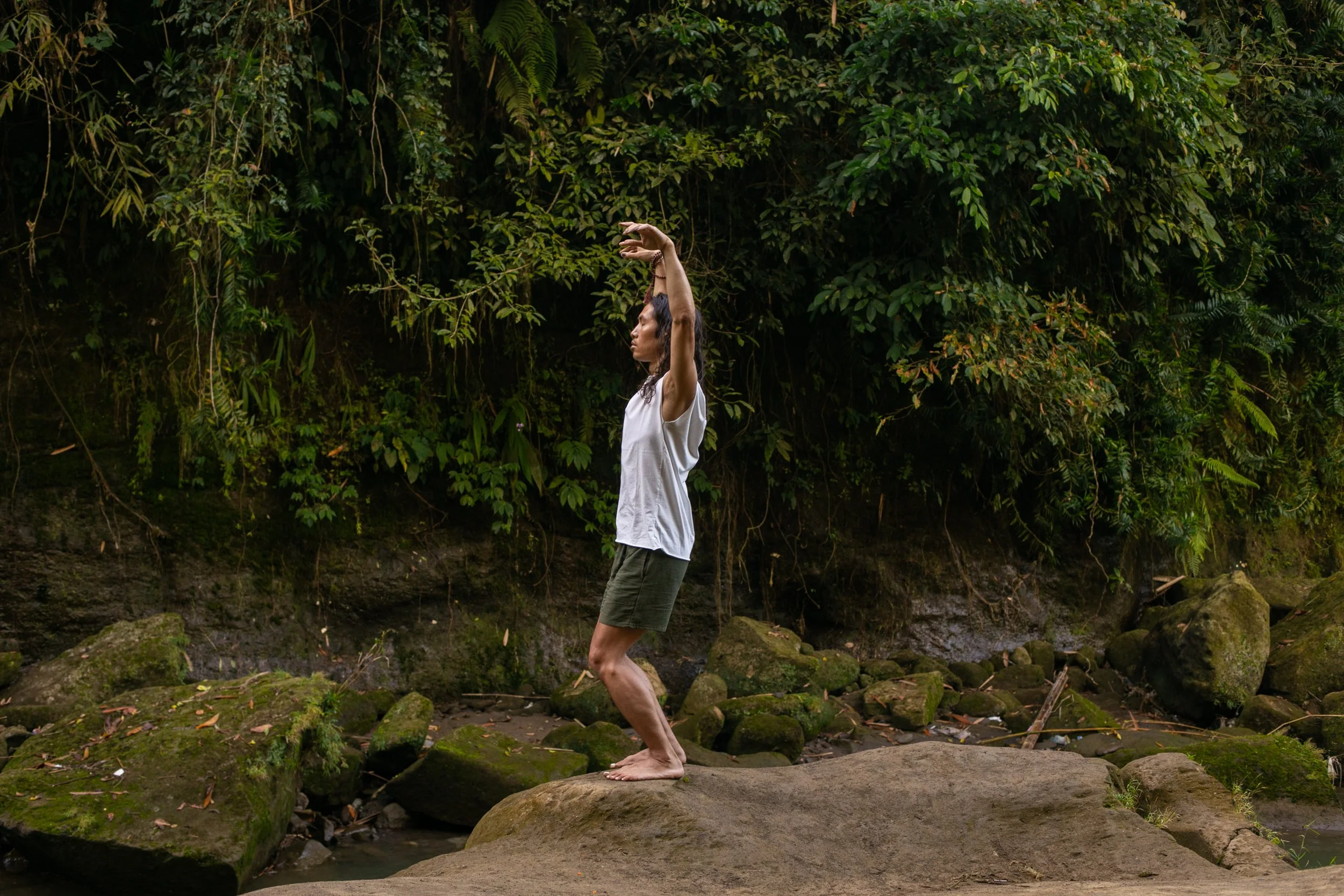 Person practicing qigong on a moss-covered rock in a lush tropical forest