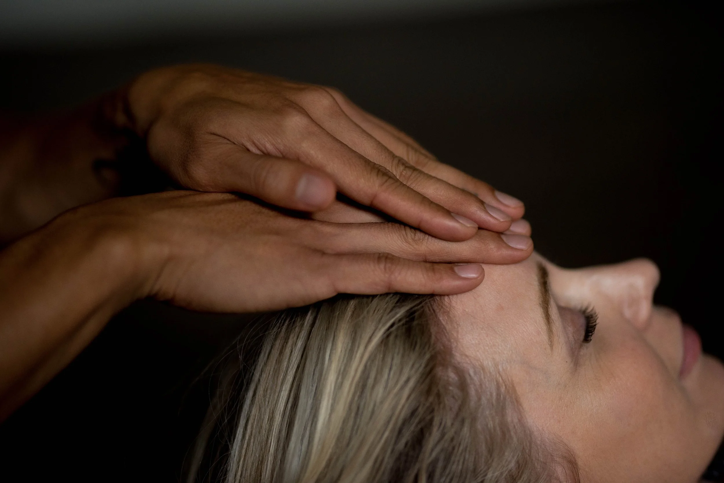 Close-up of a massage therapist’s hands applying pressure to a woman’s head