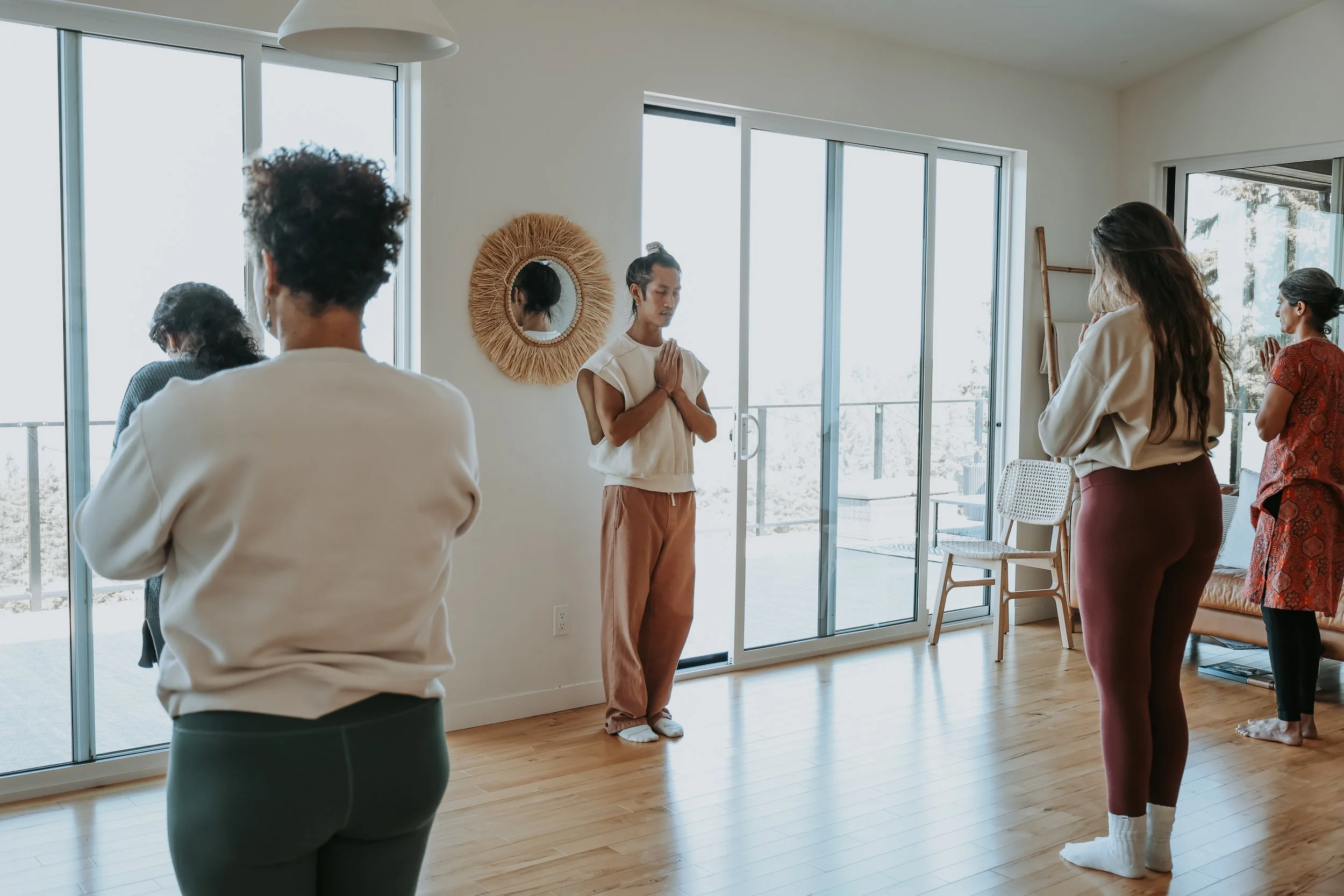 Group practicing yoga meditation with hands in prayer pose in a bright, spacious room