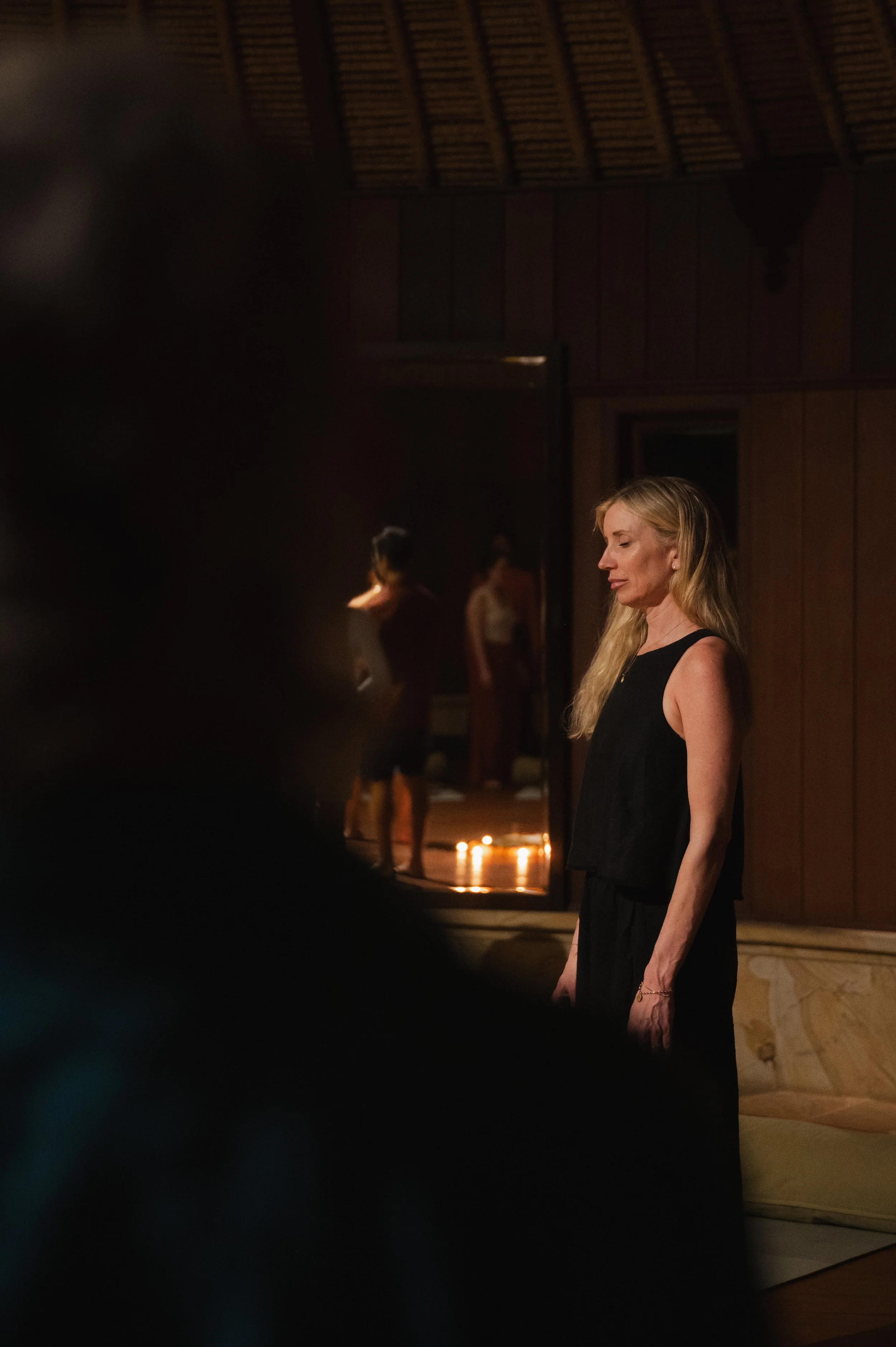 Blonde woman in a black dress standing in a dimly lit room with candles