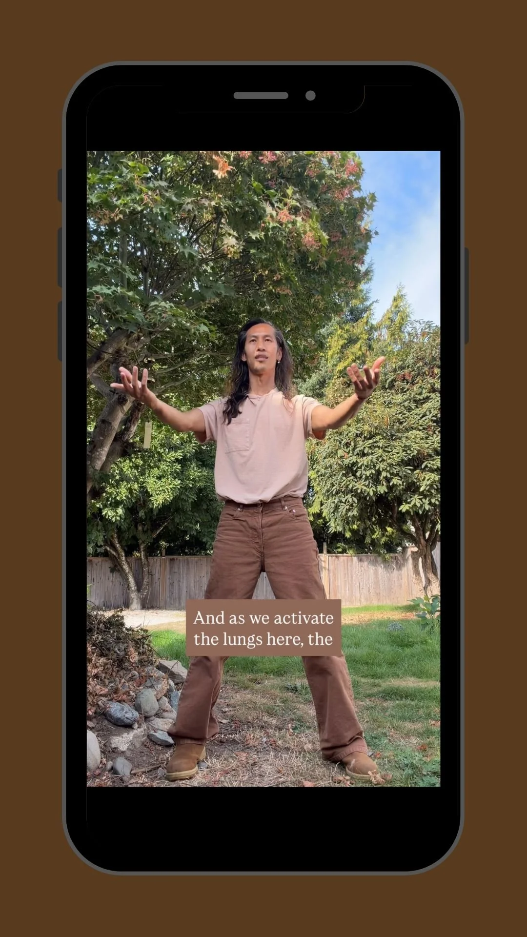 Man demonstrating a breathing exercise outdoors with arms raised in a leafy backyard; caption reads, “And as we activate the lungs here.”