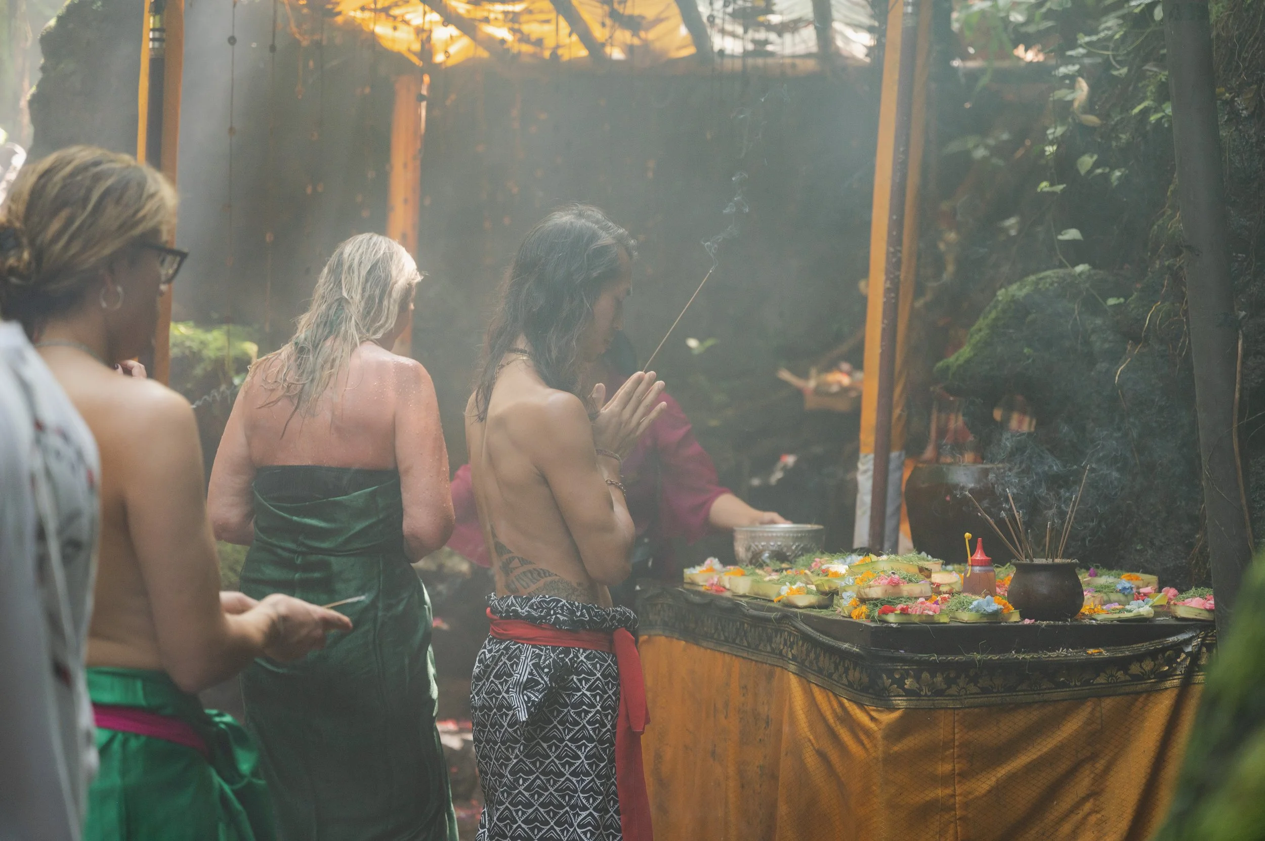 People gathered at a tropical outdoor altar with incense and colorful flower offerings