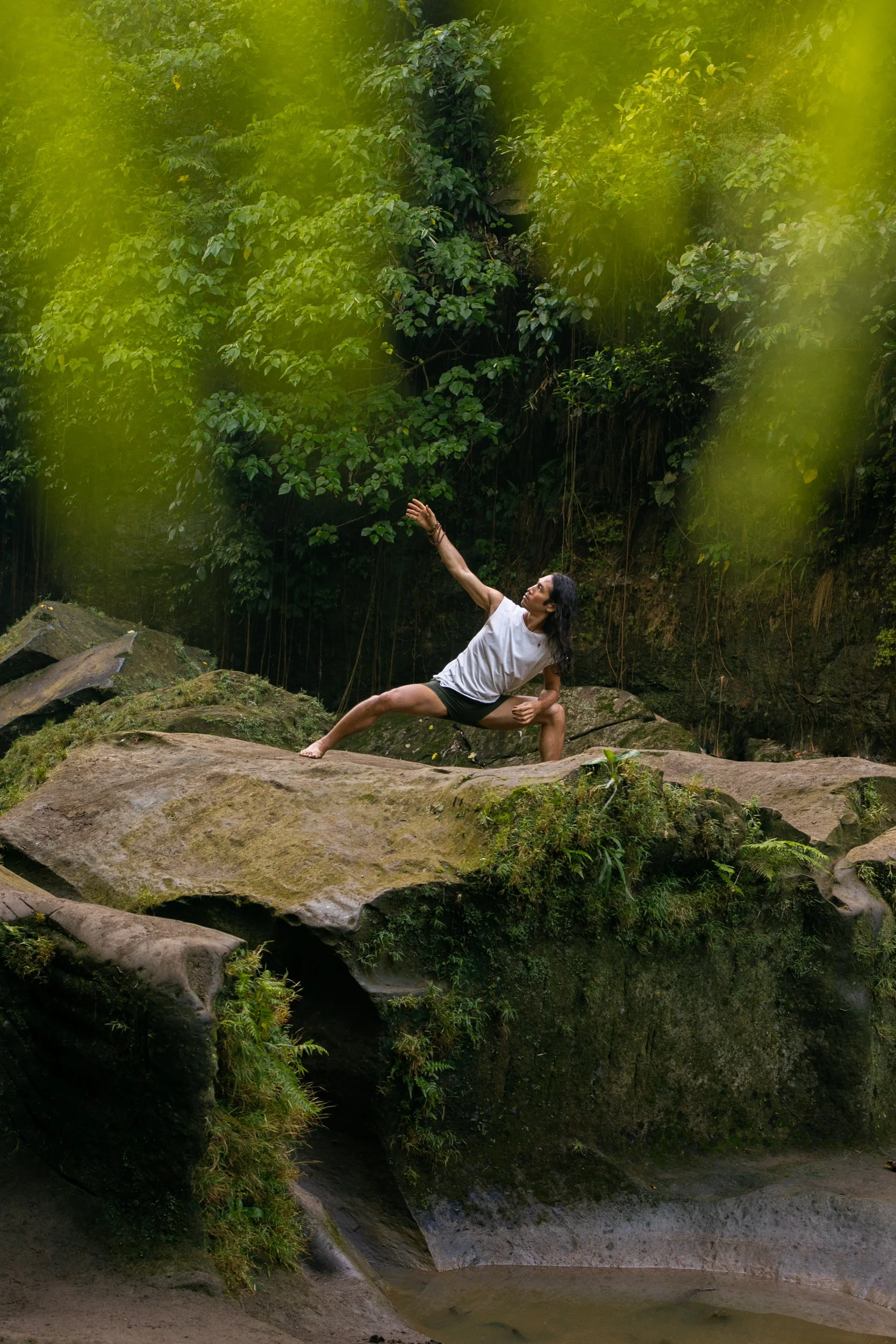 Person practicing extended side angle yoga pose on mossy rocks in a lush tropical forest