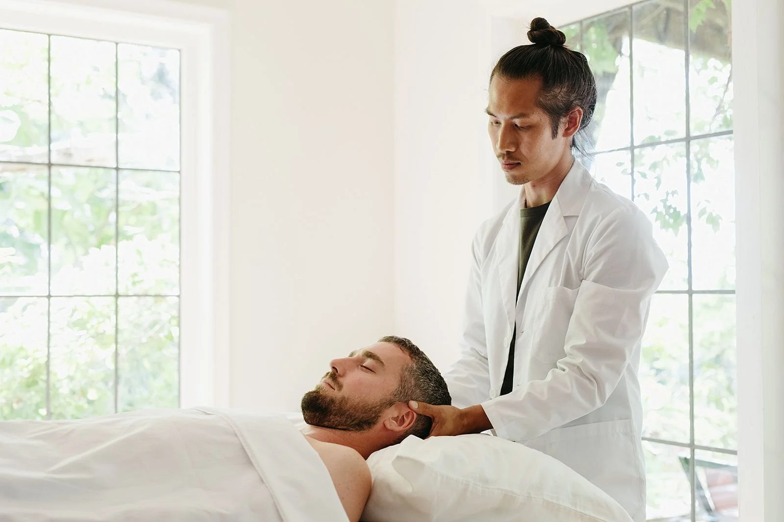 Healthcare practitioner performing a neck examination on a bearded man lying on a treatment table