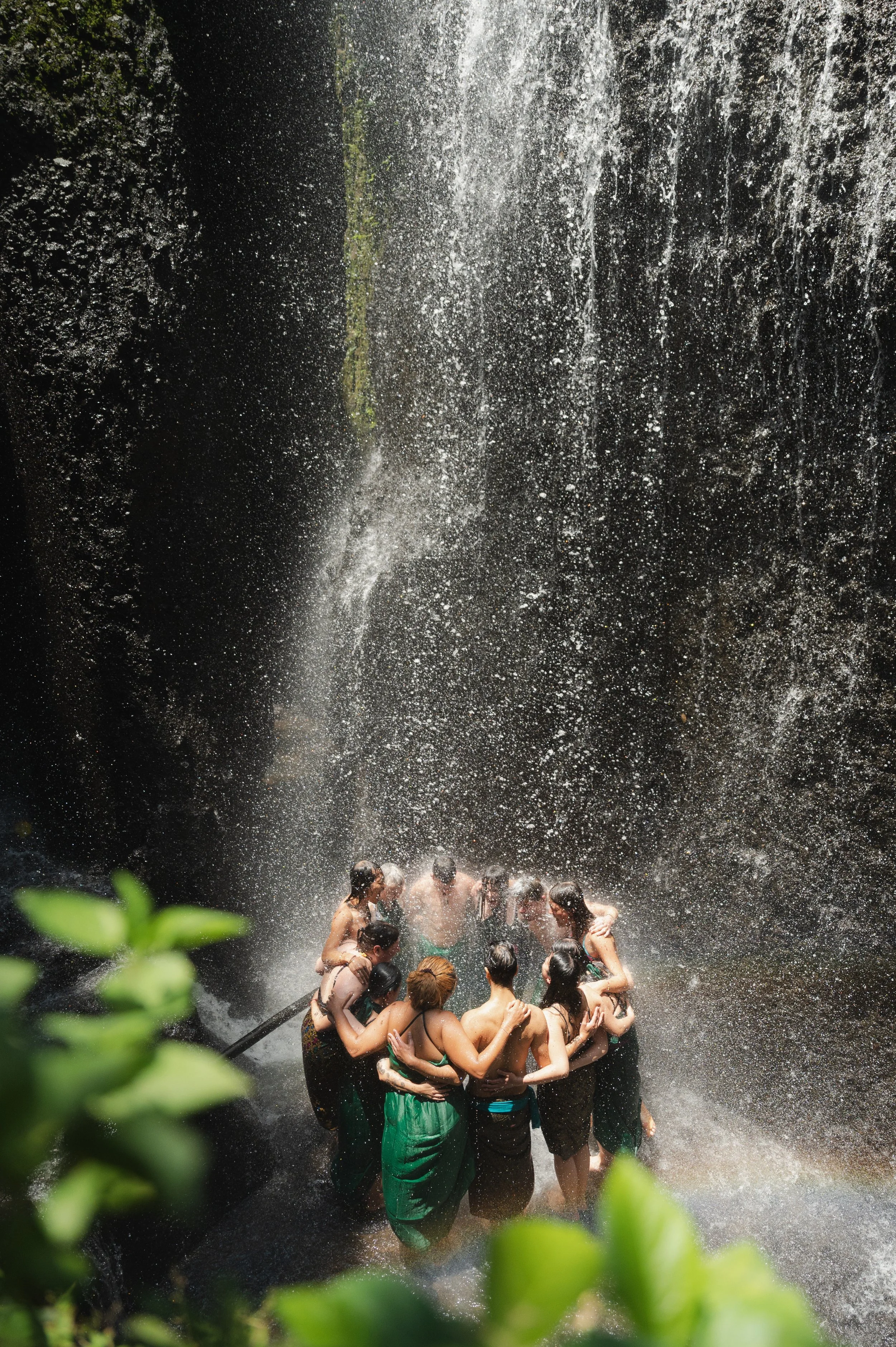 Group of people cooling off beneath a powerful waterfall in a lush forest
