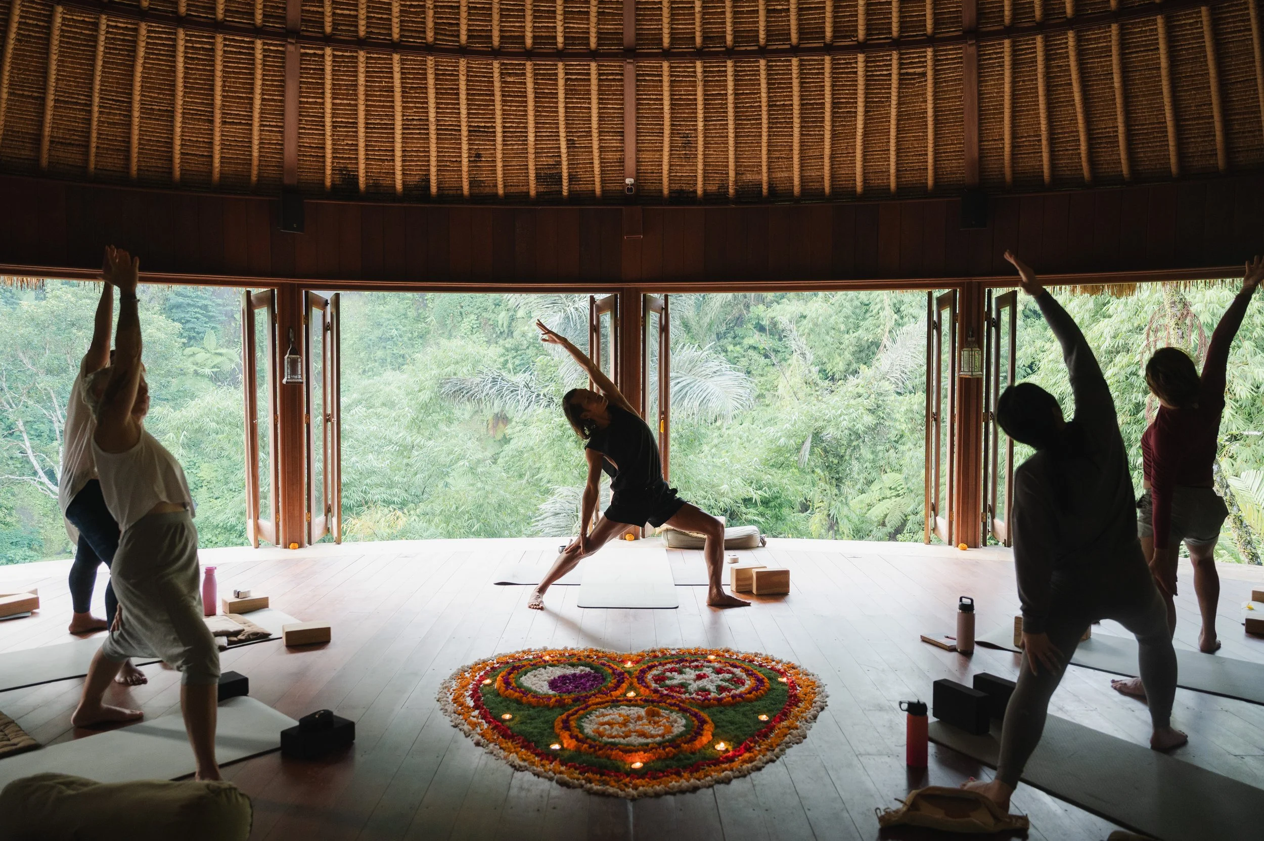Group yoga class practicing side-angle poses in an open-air pavilion surrounded by lush tropical greenery