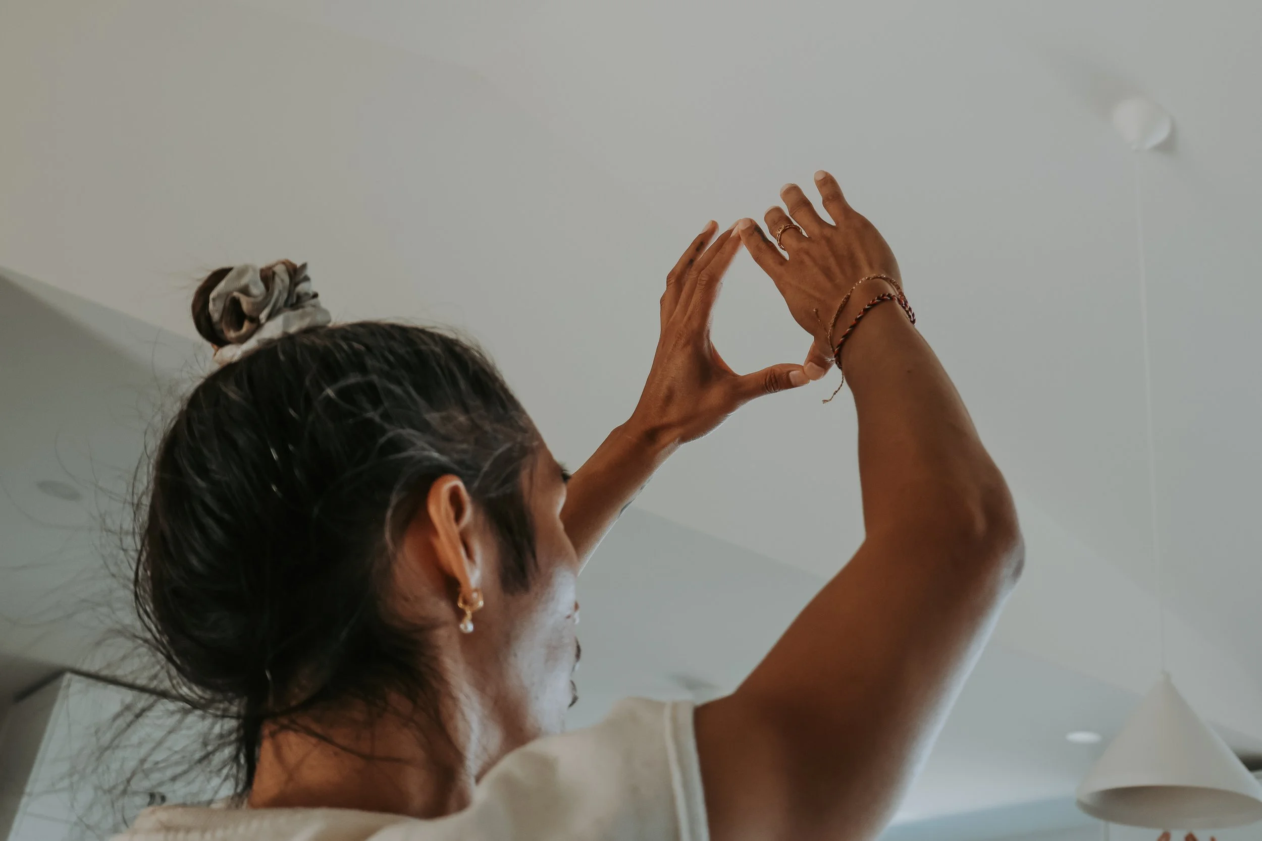 Person with hair in a bun reaching toward a ceiling light fixture