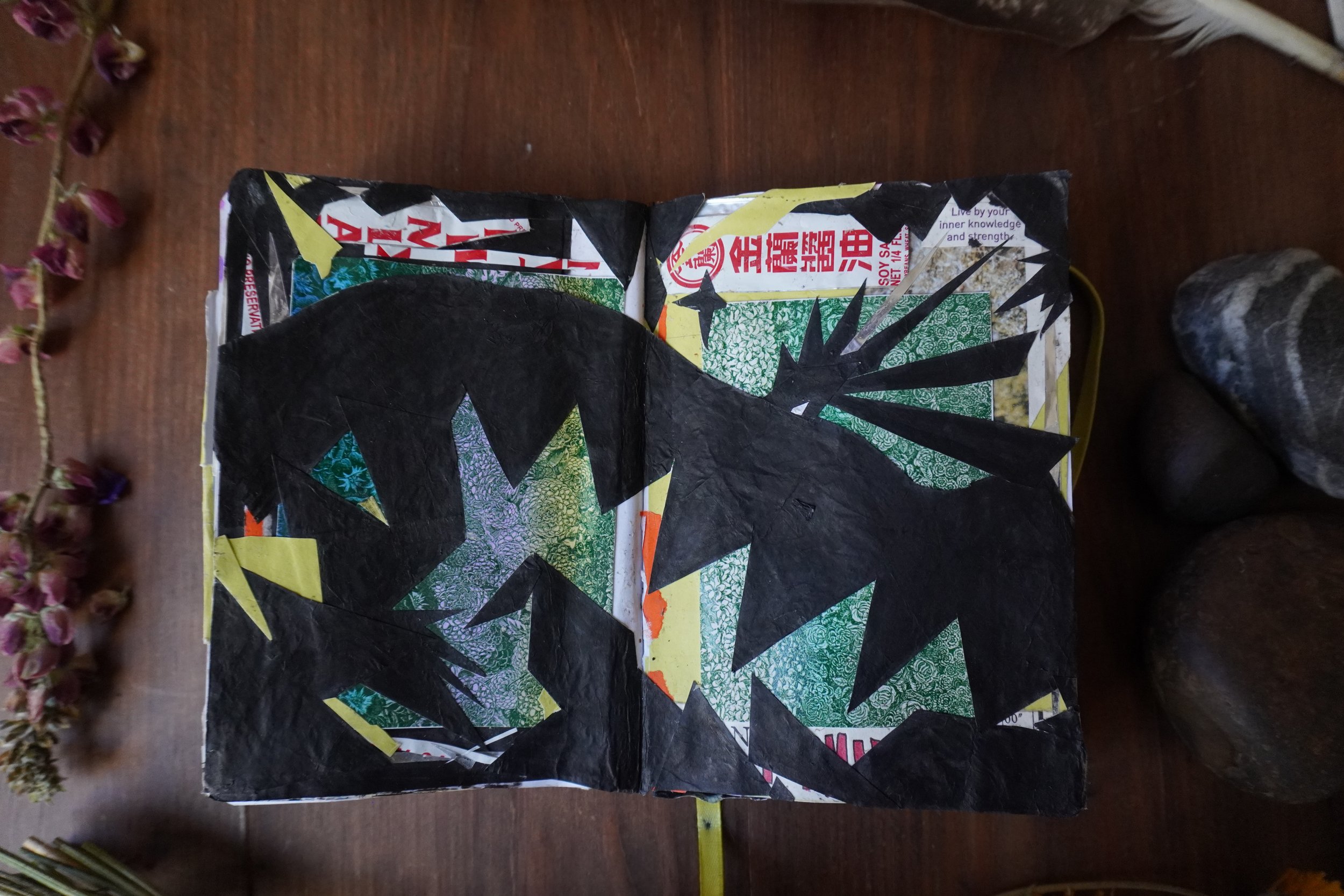 Abstract black, green, yellow, and patterned collage artwork made from repurposed packaging on a wooden table.