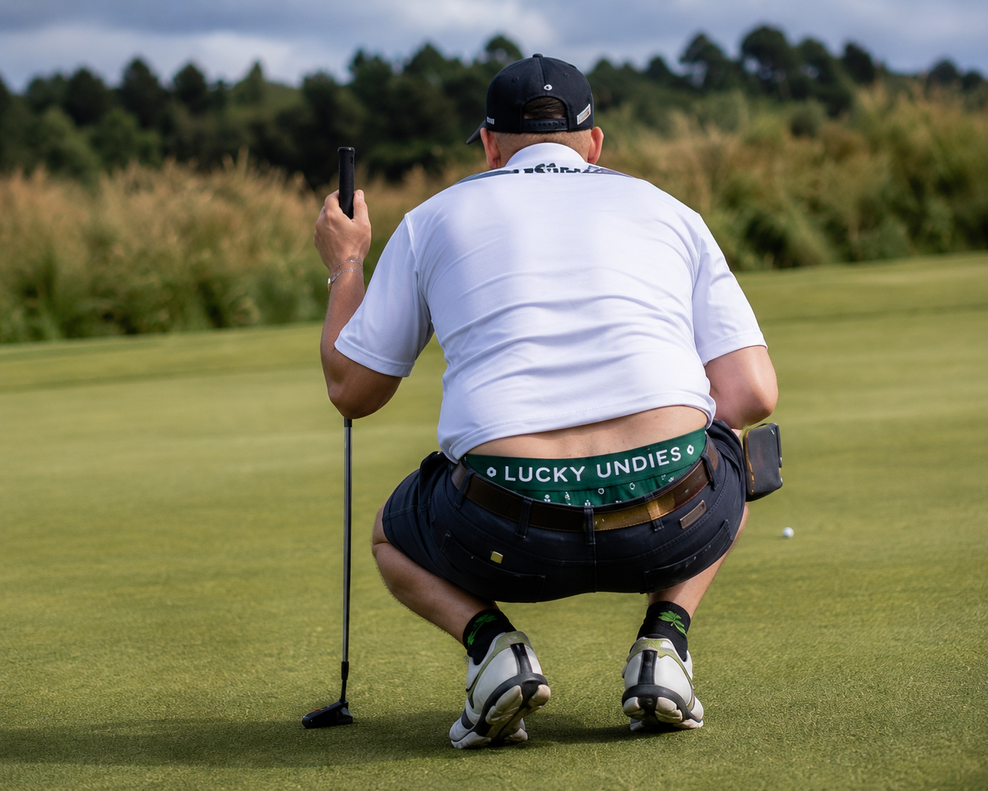 Golfer lining up a putt with a green Lucky Undies waistband visible.
