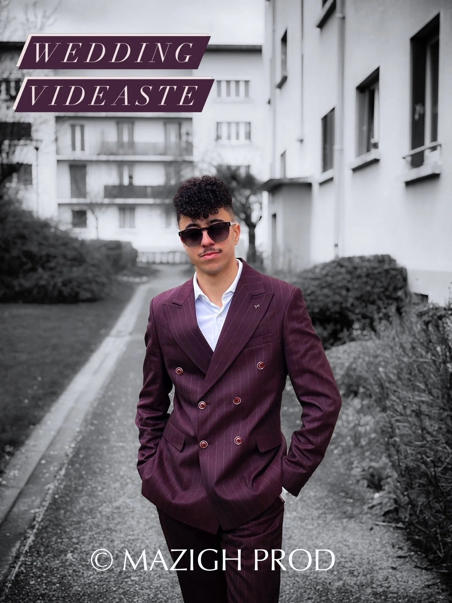 Un homme portant un costume marron à rayures et des lunettes de soleil pose dans une rue urbaine. Le fond est en noir et blanc, tandis que l'homme et ses vêtements sont en couleur.