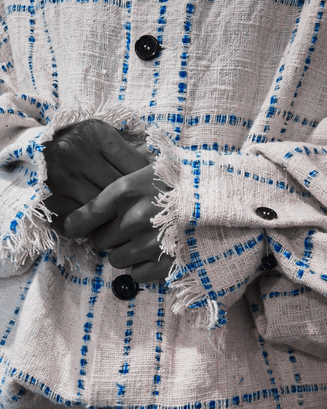 Close-up of a person's hand holding a small, newborn puppy with closed eyes. The person is wearing a white, blue-striped, frayed-edge button-up shirt.