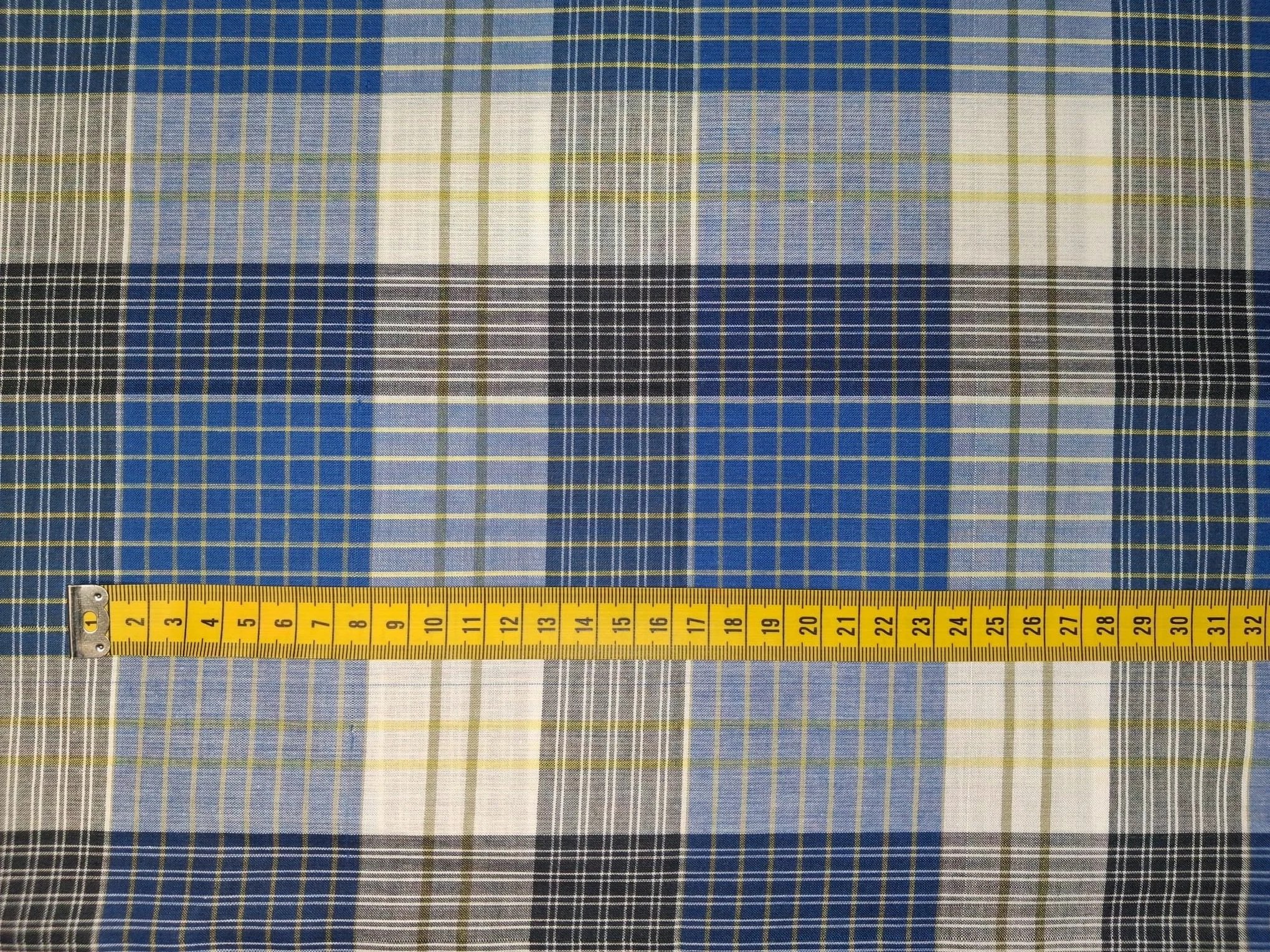 Close-up of a fabric with a multi-colored plaid pattern in shades of blue, yellow, white, black, and gray, with a yellow measuring tape laid across.