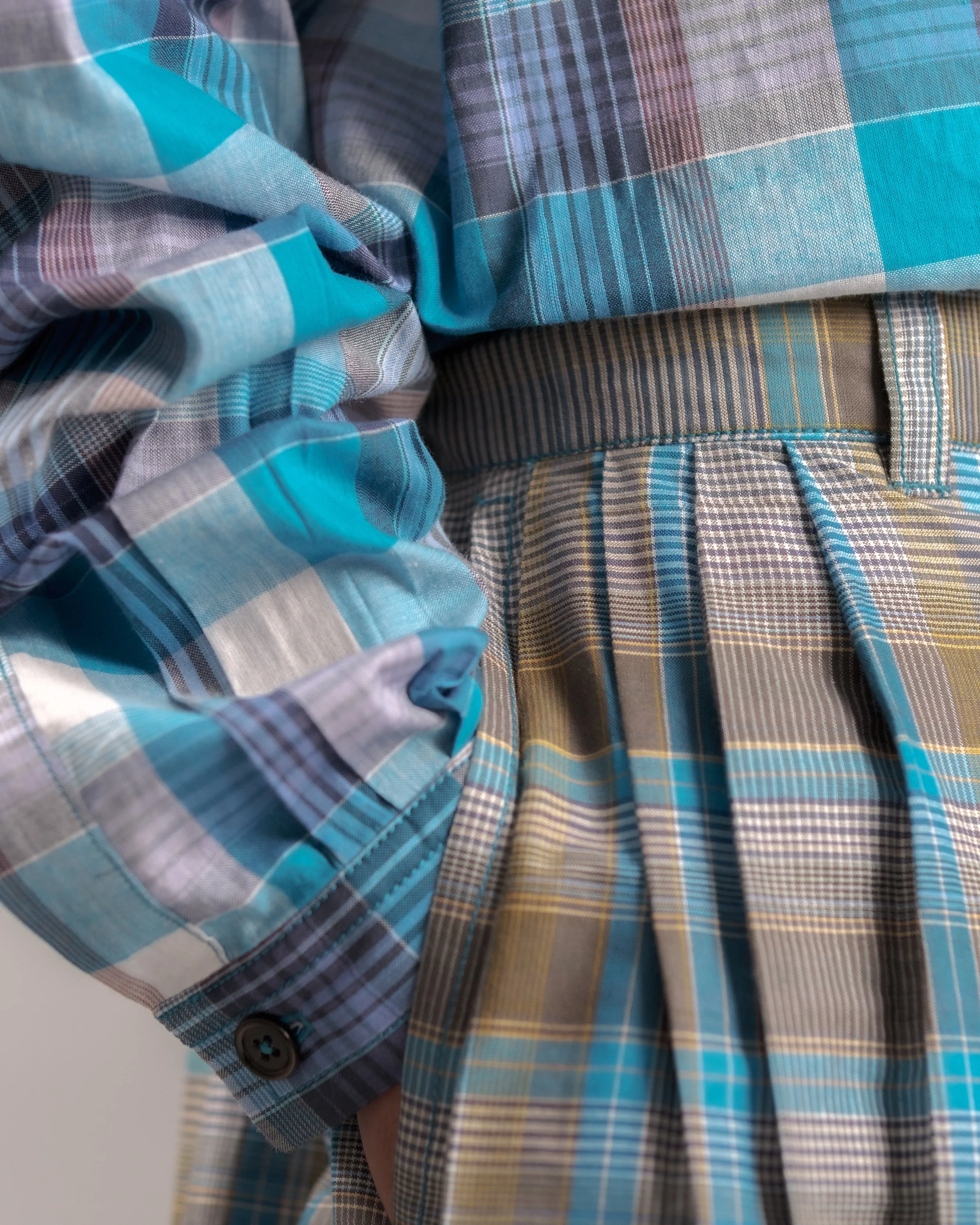 Close-up of men's plaid shirts in shades of blue, gray, and yellow, with details of fabric patterns and button cuffs.