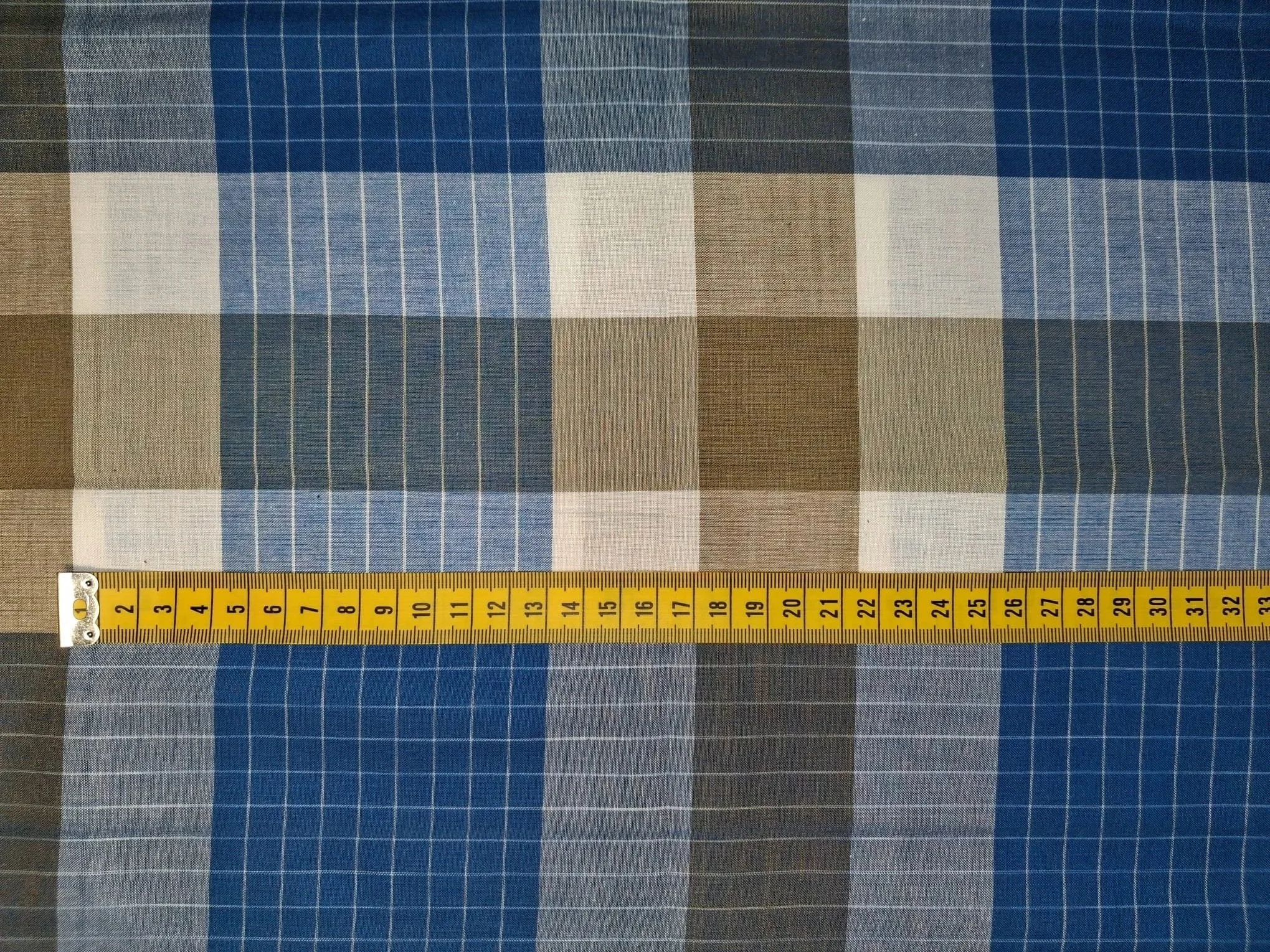 Close-up photo of a fabric with a blue, beige, black, and white checkered pattern next to a yellow measuring tape showing measurements from 1 to 33 inches.