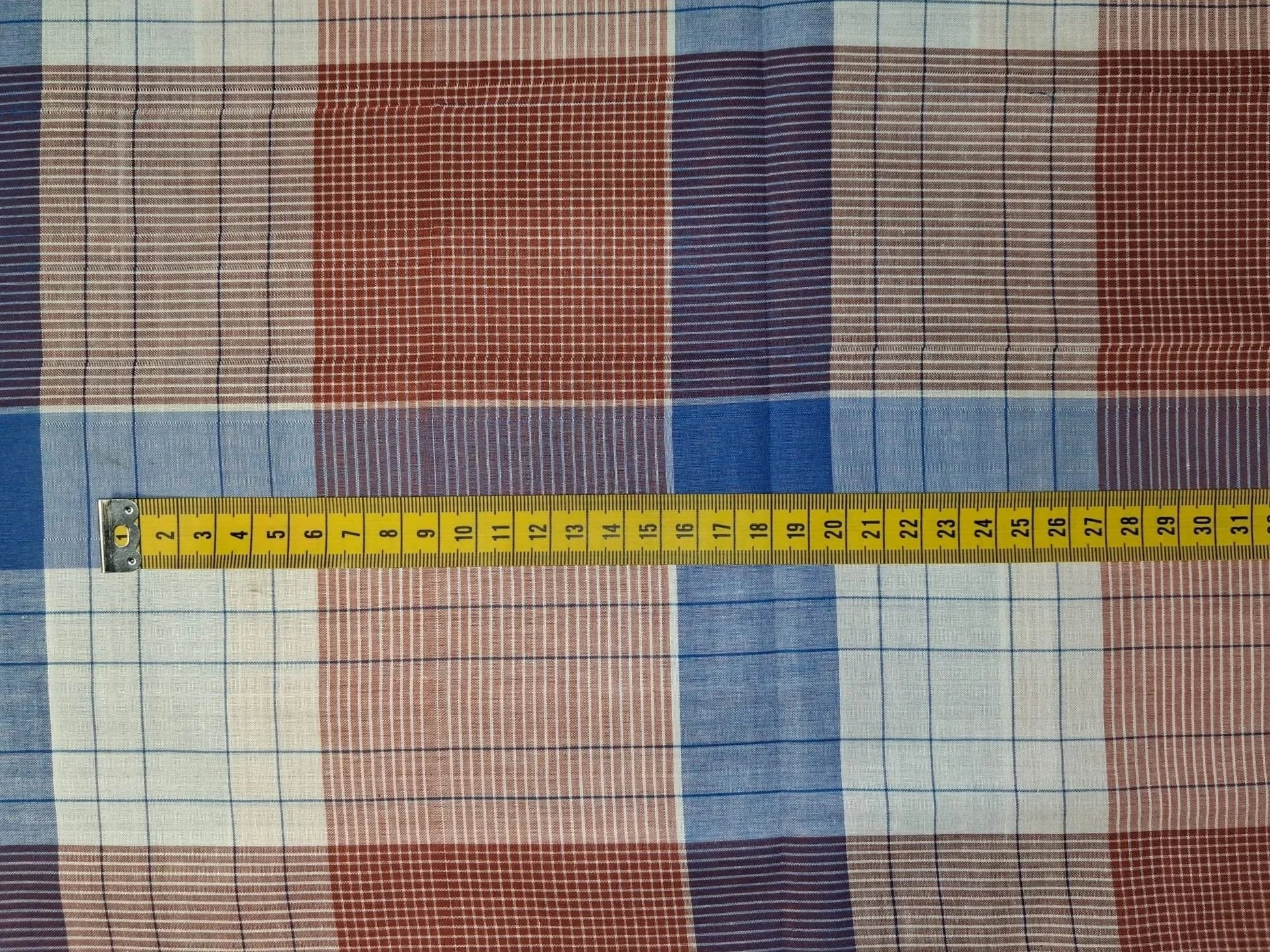 Close-up of a fabric with red, blue, and white checkered pattern, and a yellow measuring tape laid across it with measurements in inches.