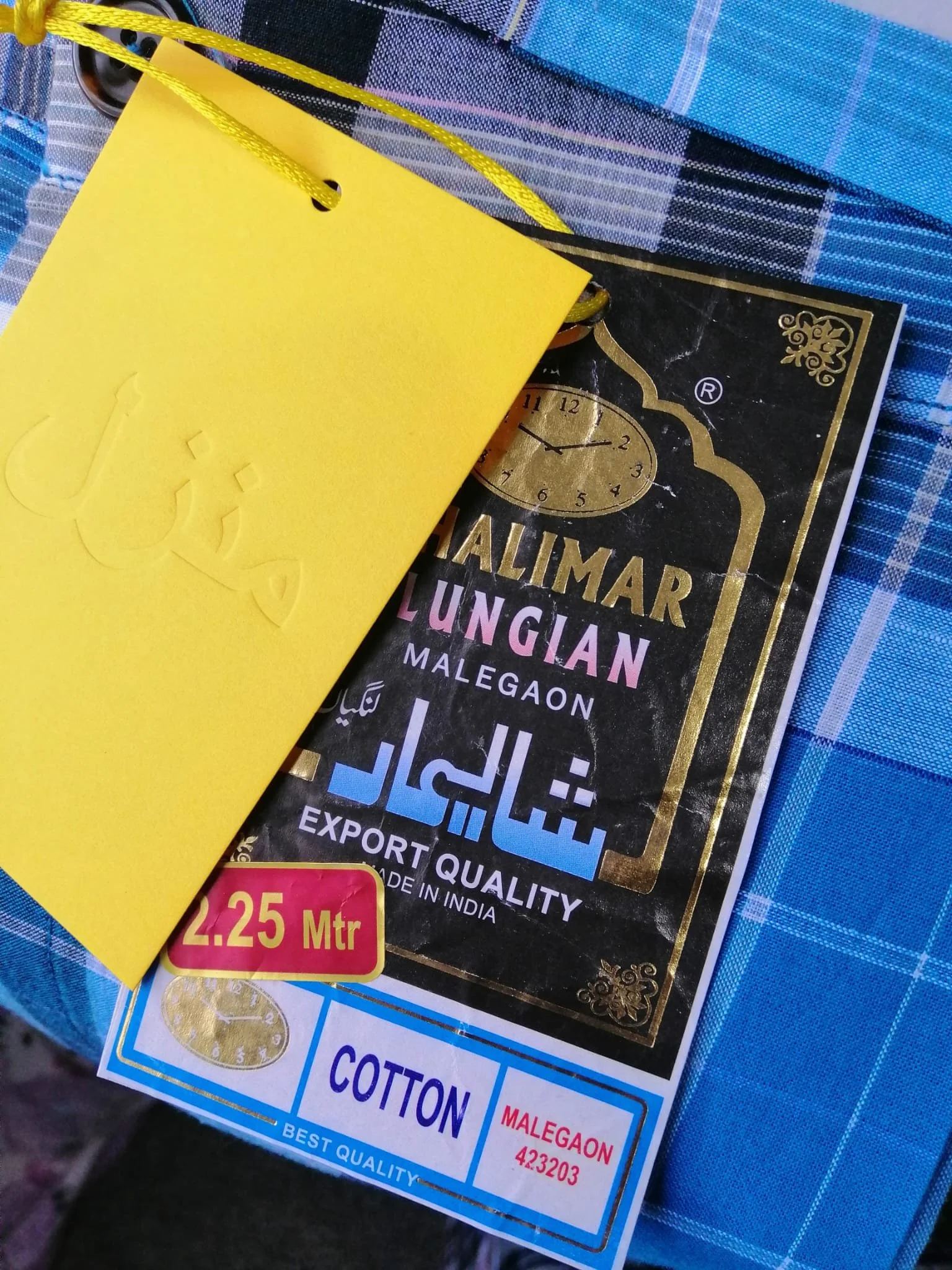 Close-up of a yellow tag attached to a package of rice, with black, gold, and pink text on a black background, and a certificate of authenticity. The package label indicates it is a type of rice from India, with details about quality and origin, and a price label showing 2.25 meters.