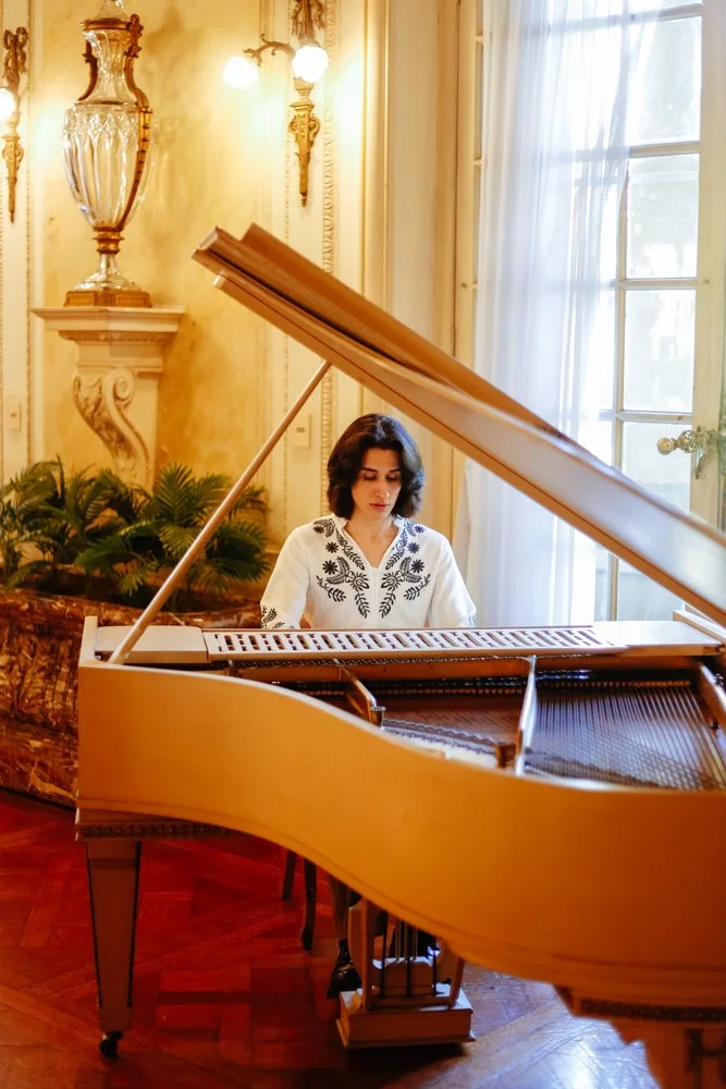 Un chico tocando un piano de cola en un salón elegante con luz natural y decoración clásica.