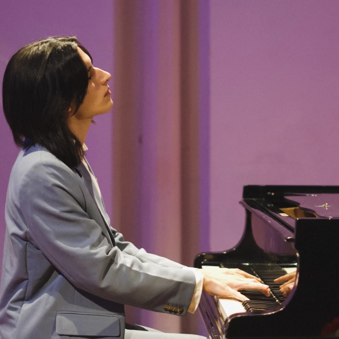 Persona tocando un piano en una sala con paredes de color lila.