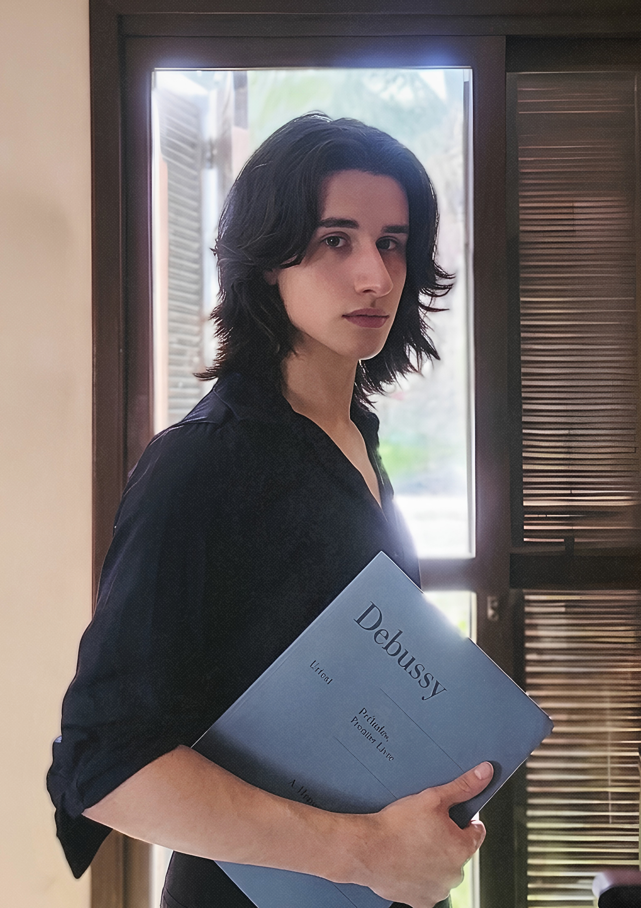 Chico de cabello medio largo posando con un libro de partituras en la mano