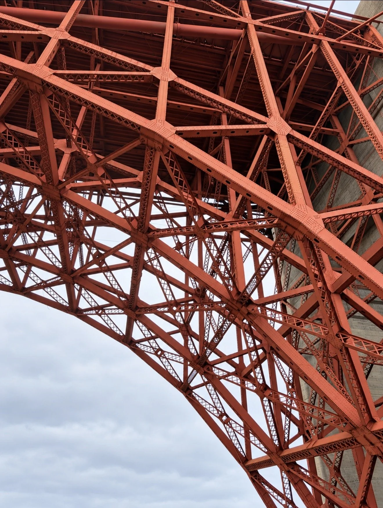 Close-up of the red steel beams beneath the Golden Gate Bridge against a cloudy sky.