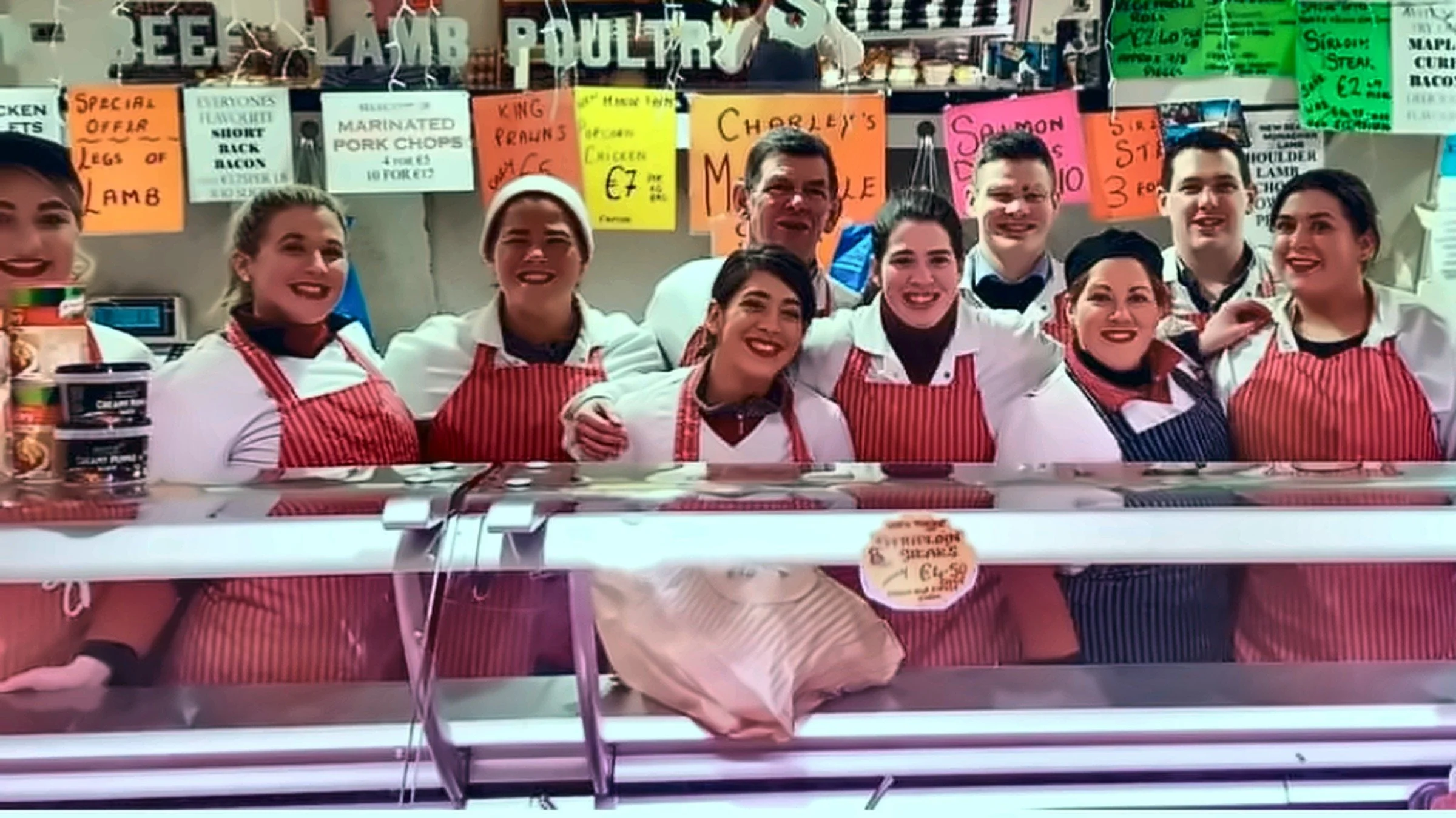 Smiling butchers in red striped aprons behind the shop counter at Charley's Meats