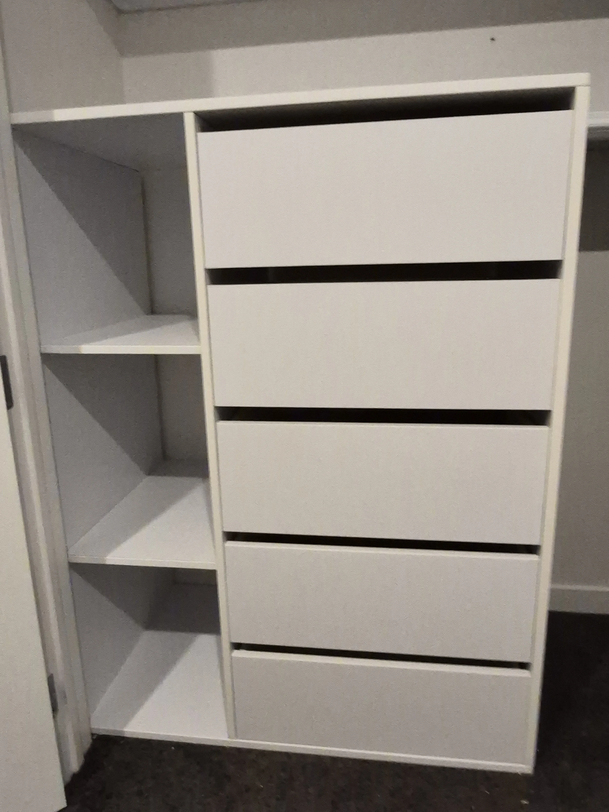 A white, empty, modern cabinet with open shelves on the left side and closed drawers on the right side, positioned against a gray wall.