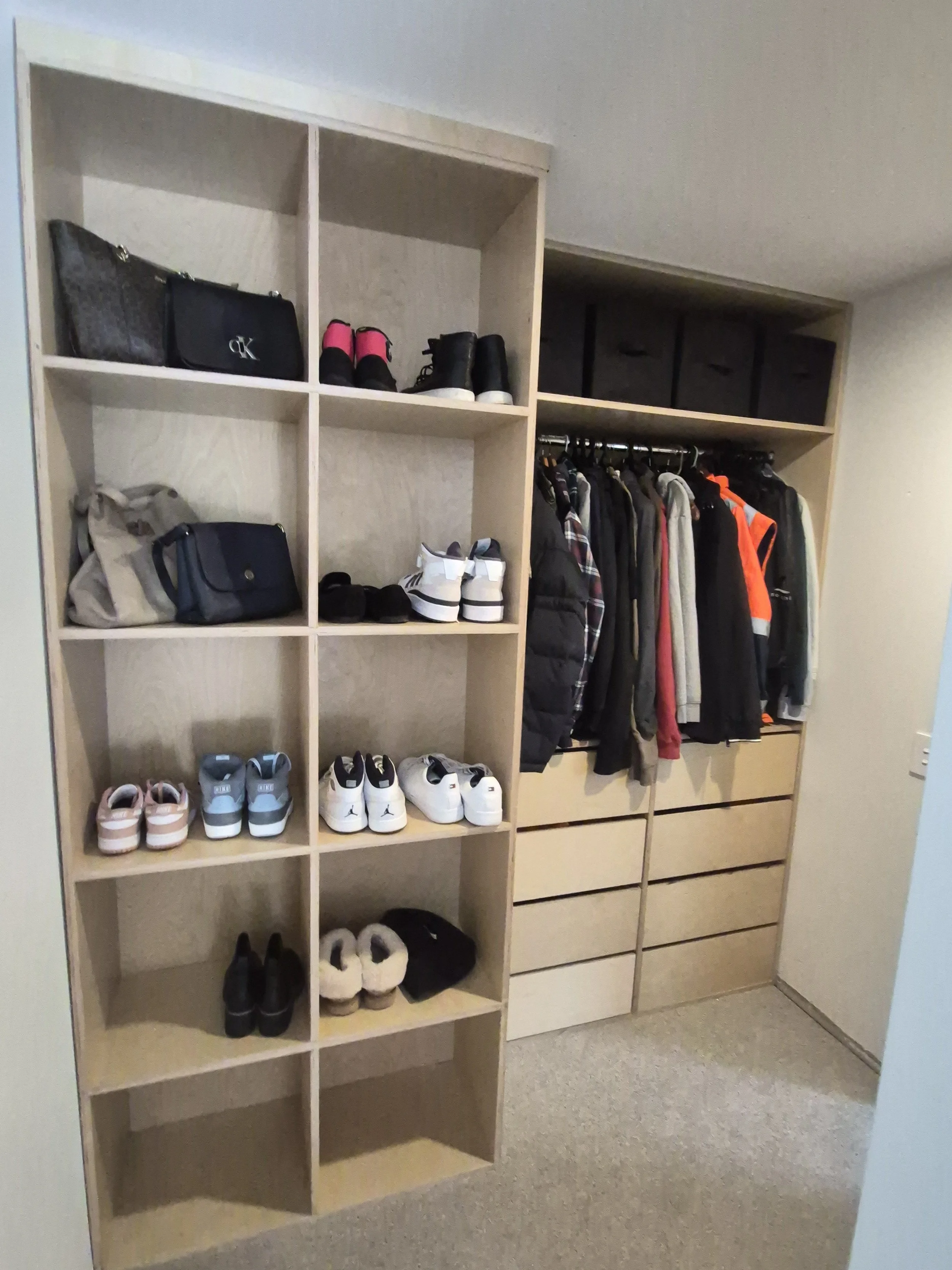 Wooden shelving unit in a closet with shoes, bags, and clothes