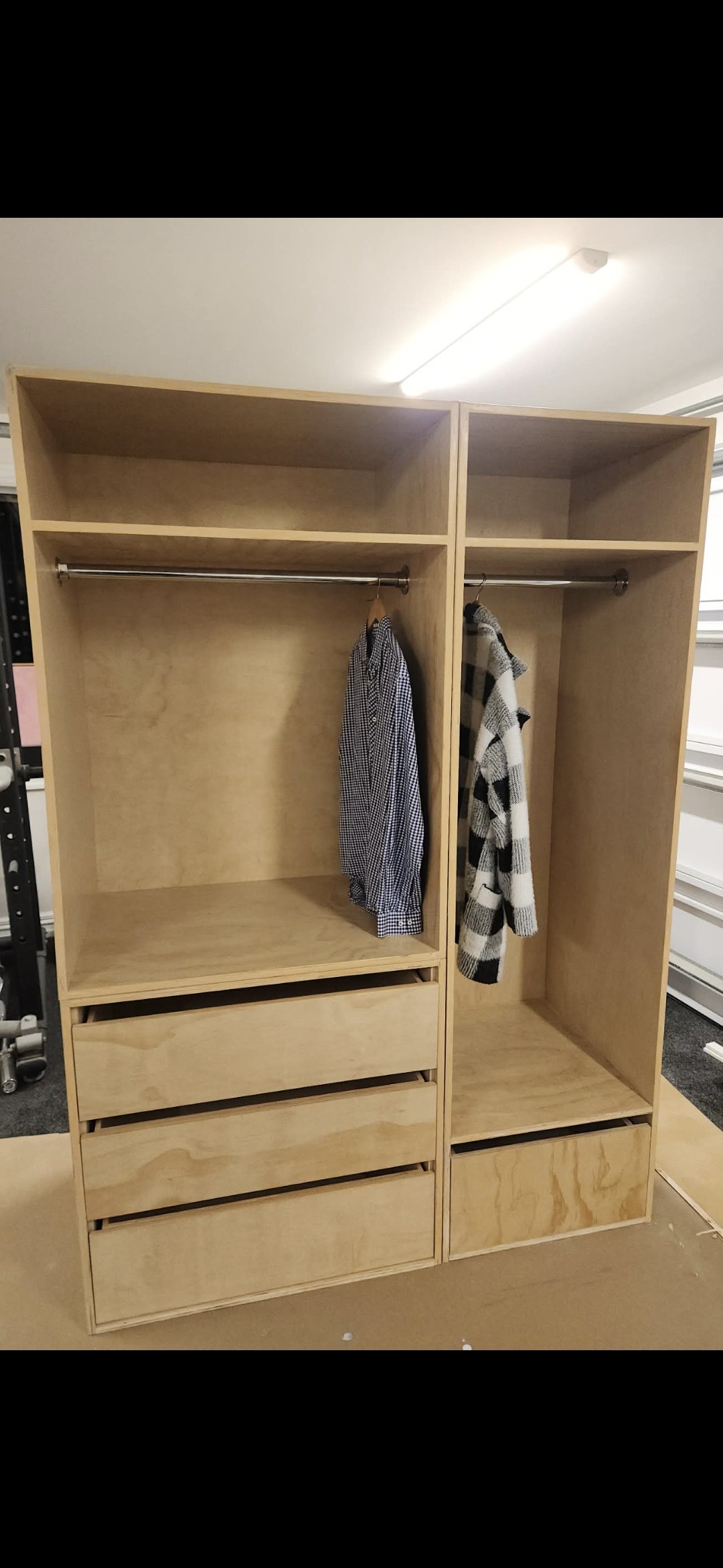 Empty wooden wardrobe with shelves and drawers, with a checkered shirt and a black and white checkered coat hanging inside.