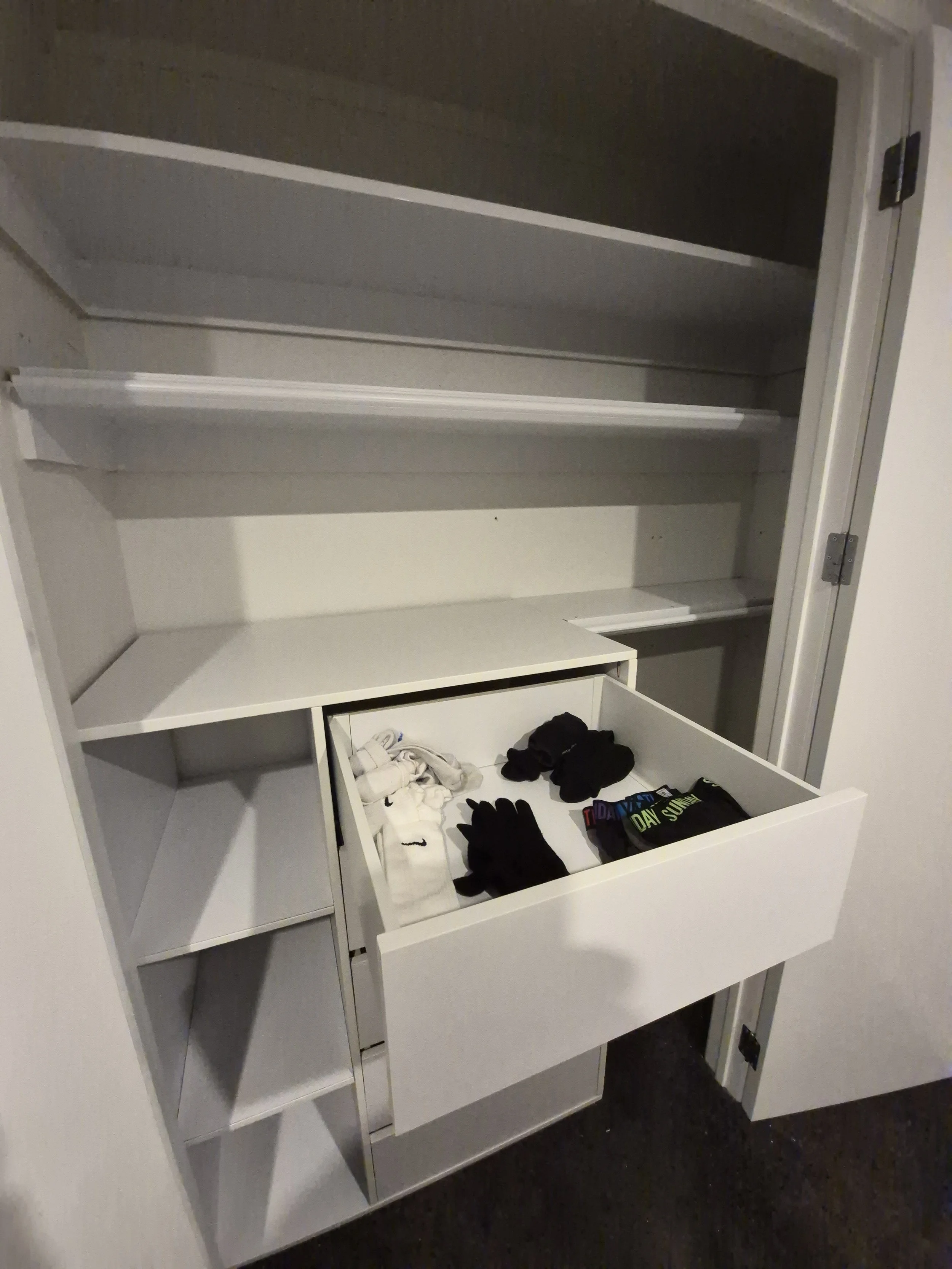 Empty white wardrobe with shelves and drawers, some clothes and gloves stored in the drawer.