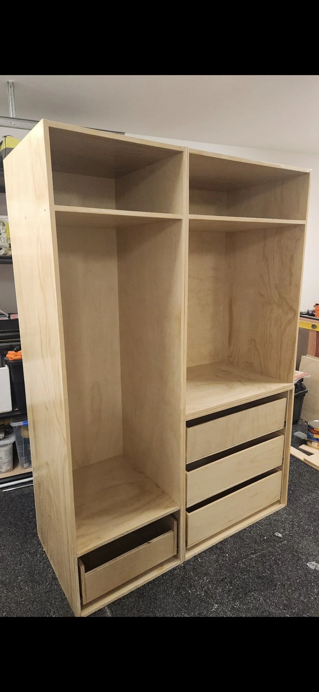 Unfinished wooden shelving unit with multiple compartments and three drawers at the bottom, sitting in a workshop.