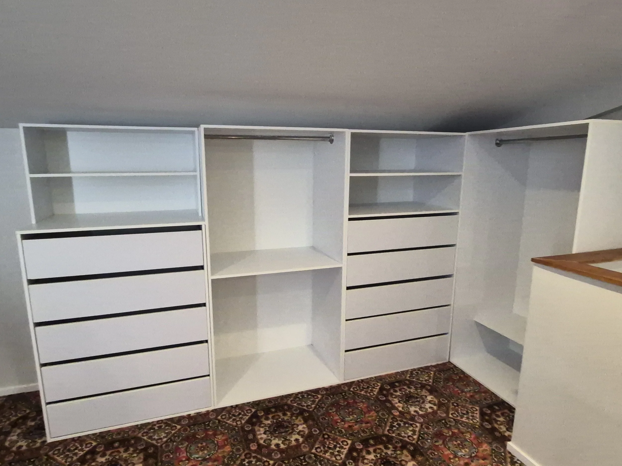 Empty white built-in closet with shelves and drawers, situated on a floral patterned rug.