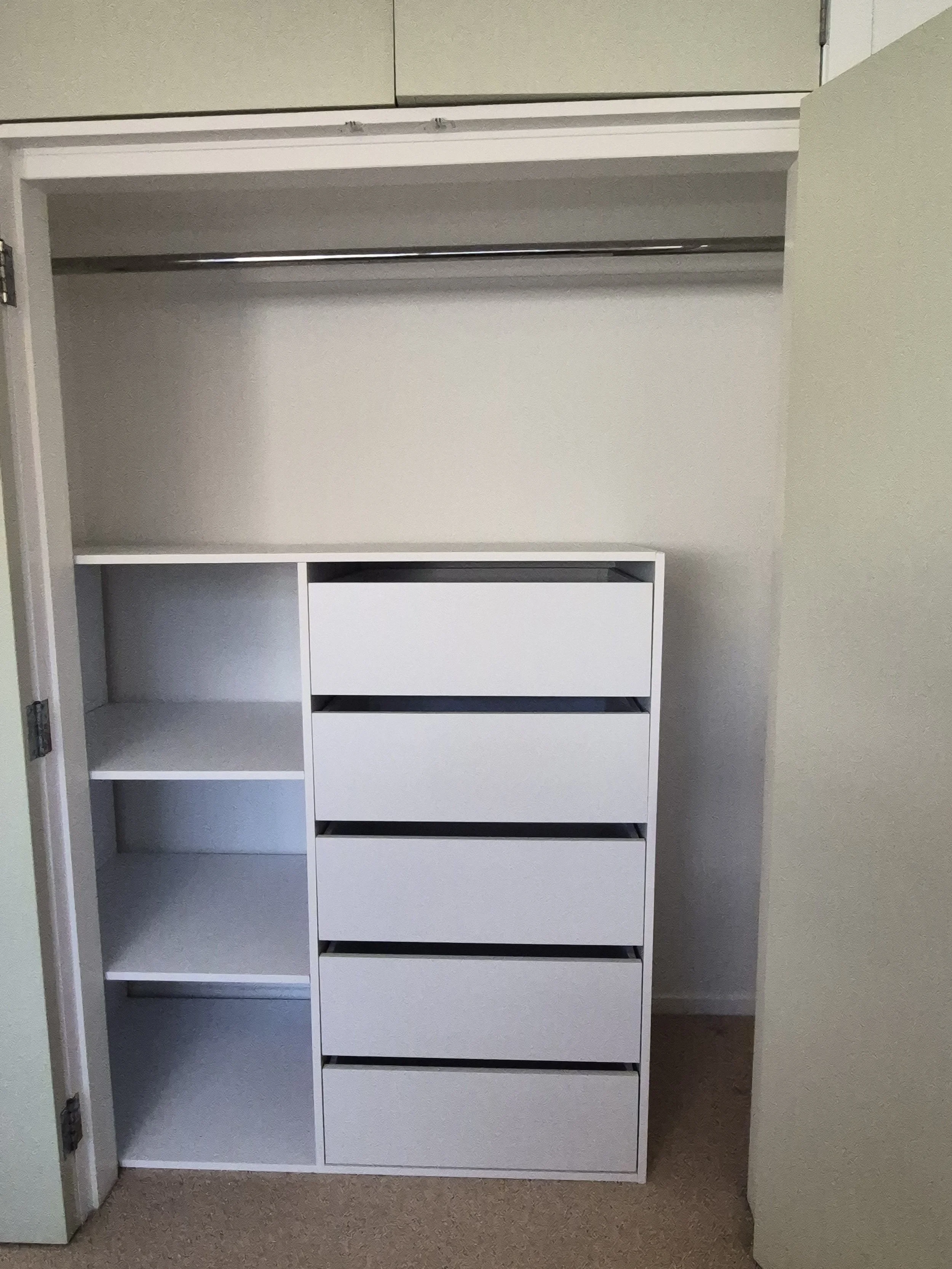 Empty white closet with shelves and drawers in a room with beige carpet and pale green walls.