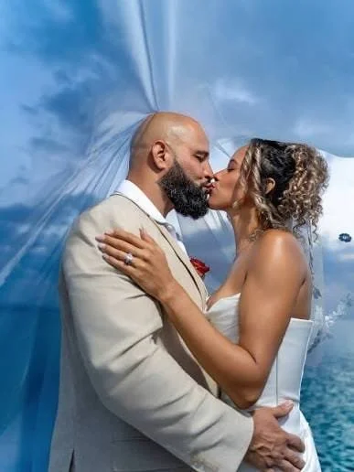 A newlywed couple sharing a kiss on their wedding day next to the ocean.